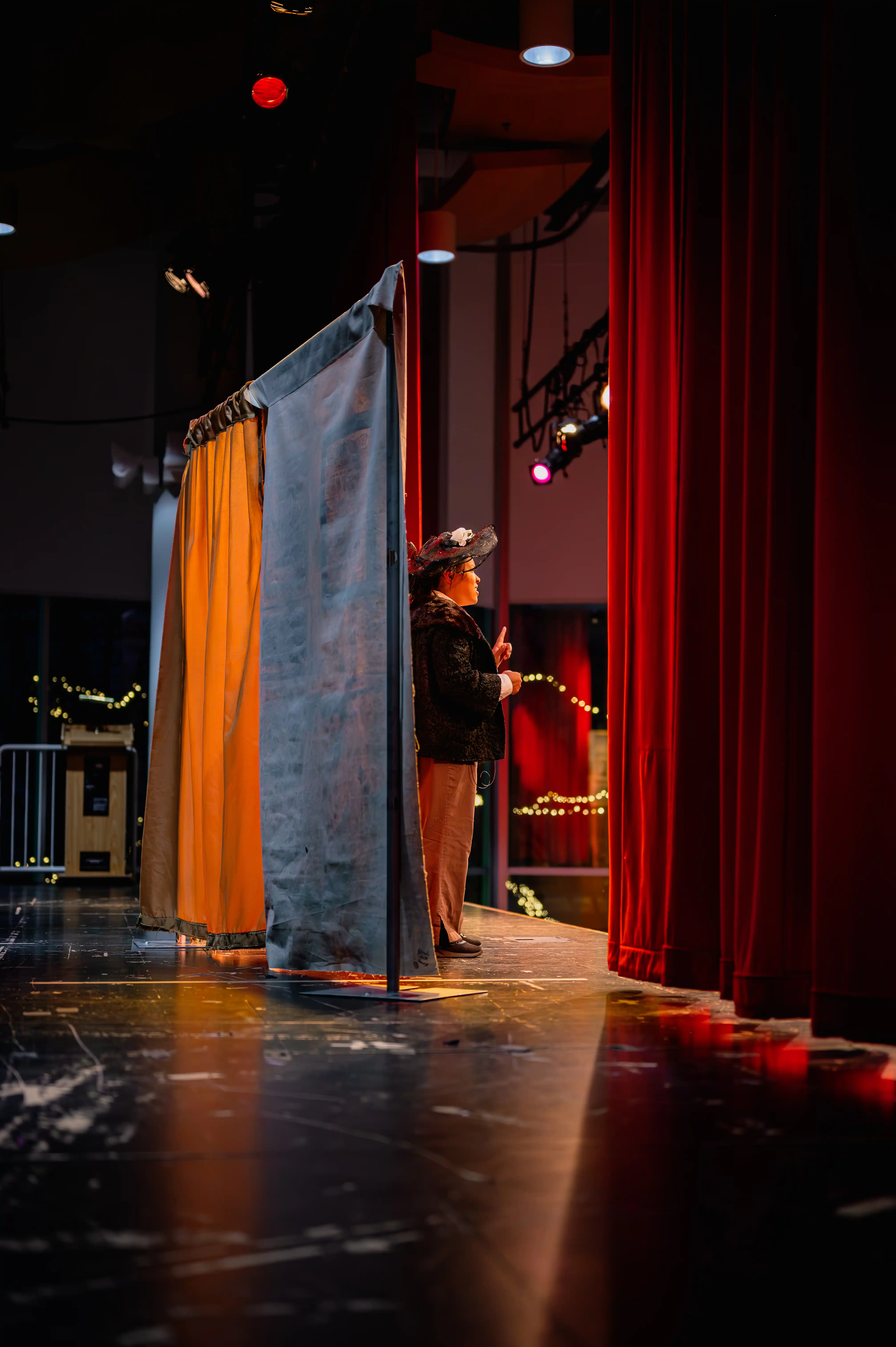 Person peeking from behind stage curtains, with stage lighting visible.