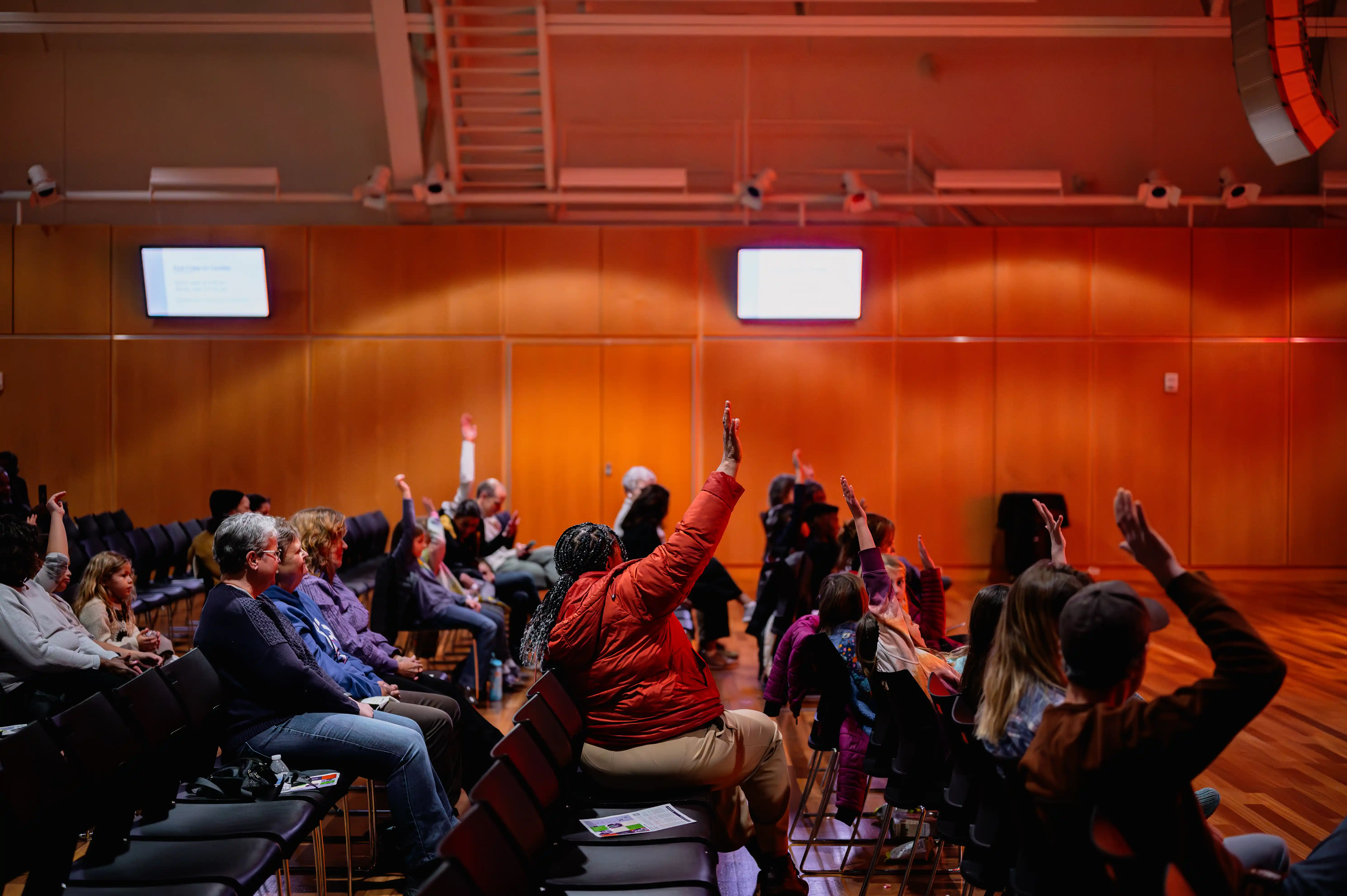 Audience members raising their hands in a conference room with warm lighting.