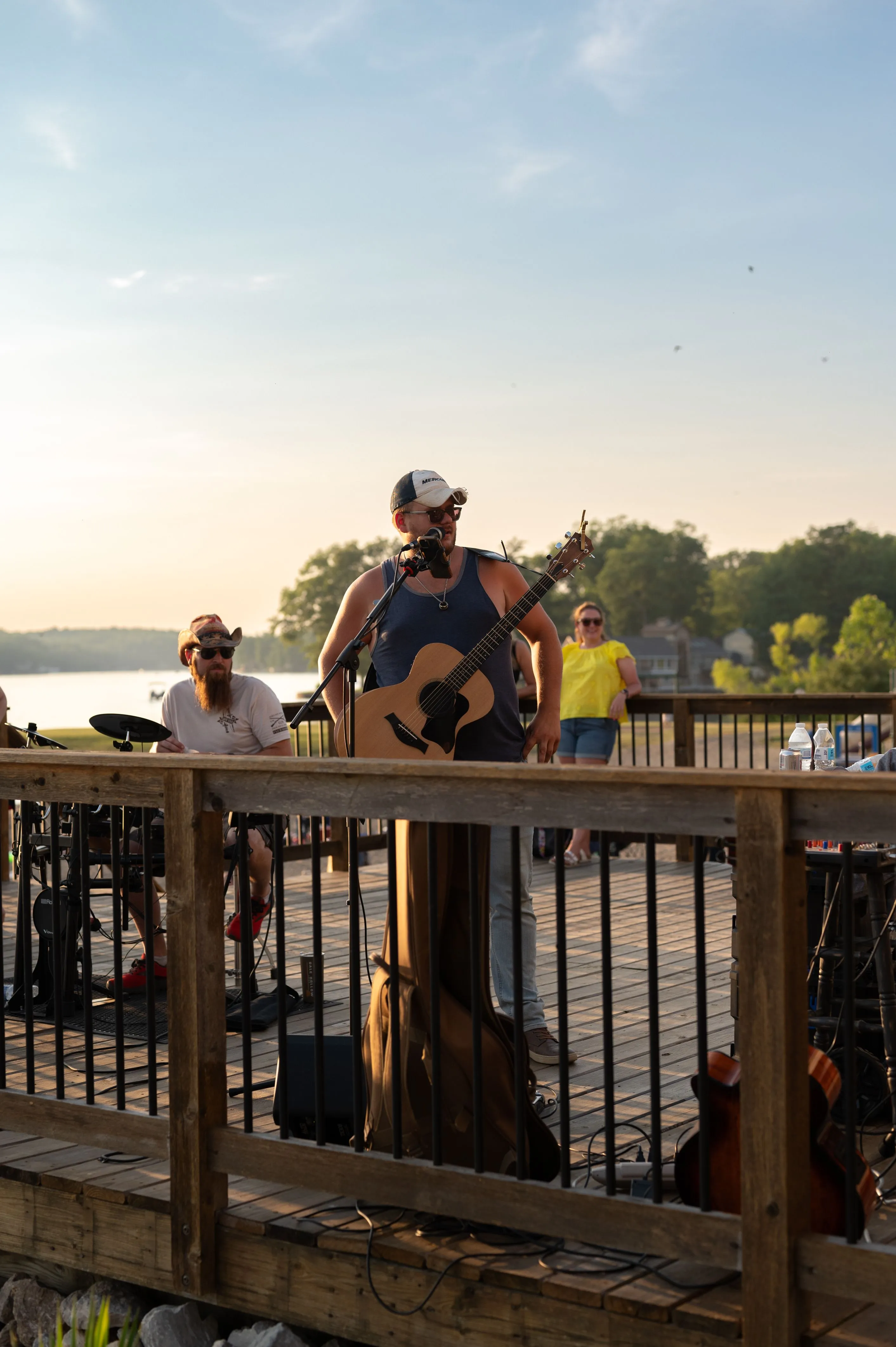 Two musicians performing on a deck by a lake at sunset.