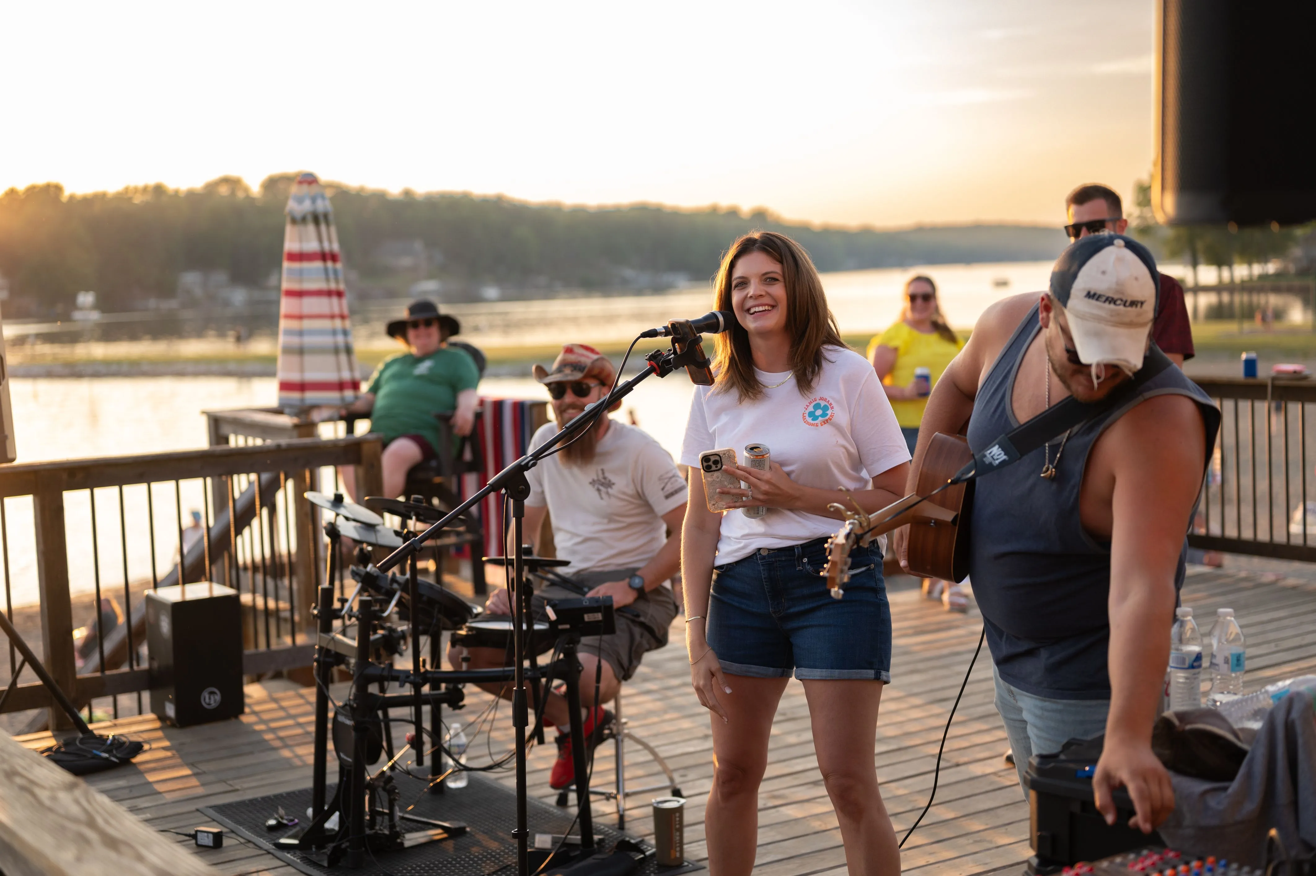 People enjoying a live music performance on a riverside boardwalk at sunset.