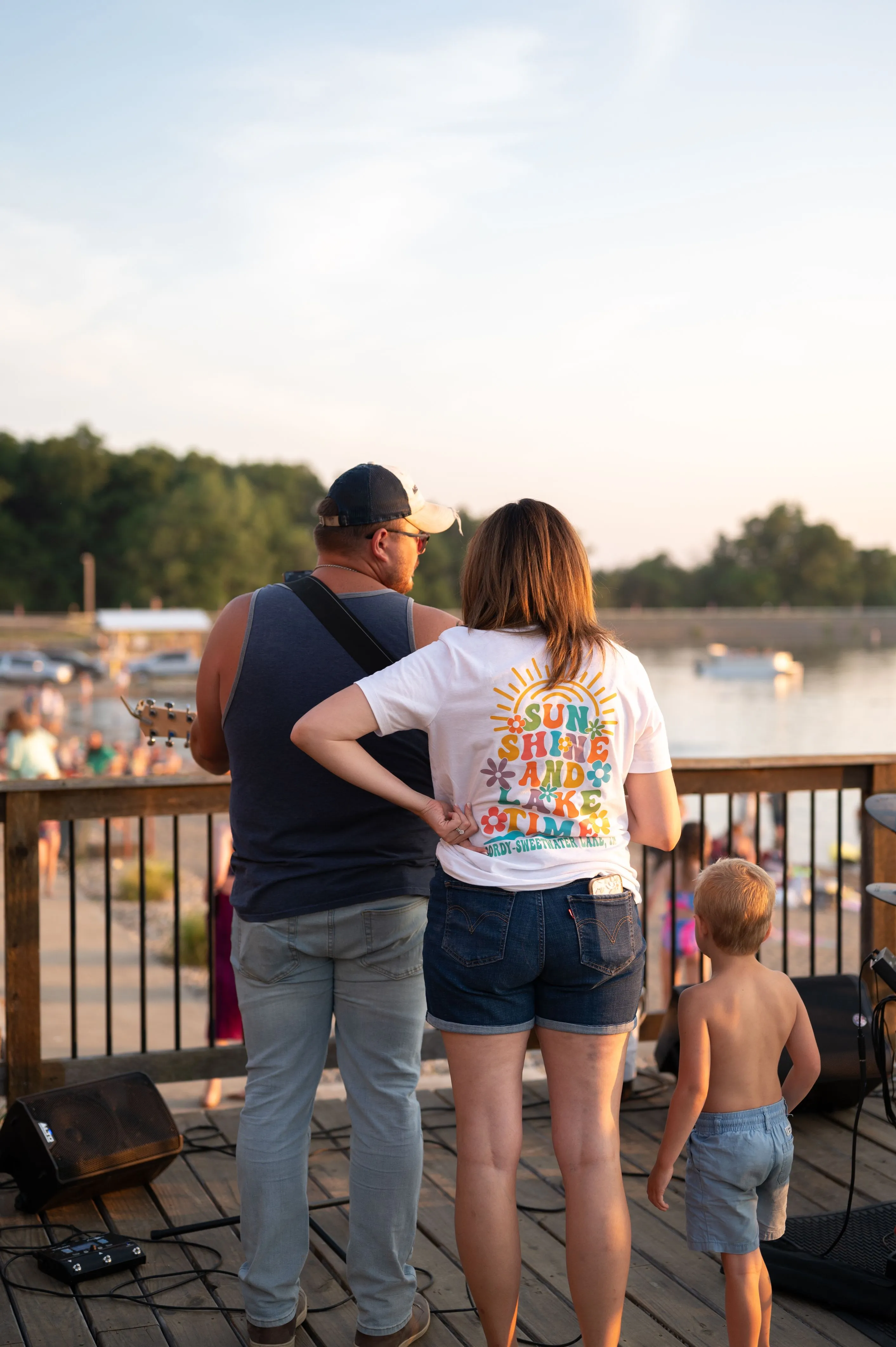 Two adults standing by a railing overlooking a body of water with a young child walking nearby.