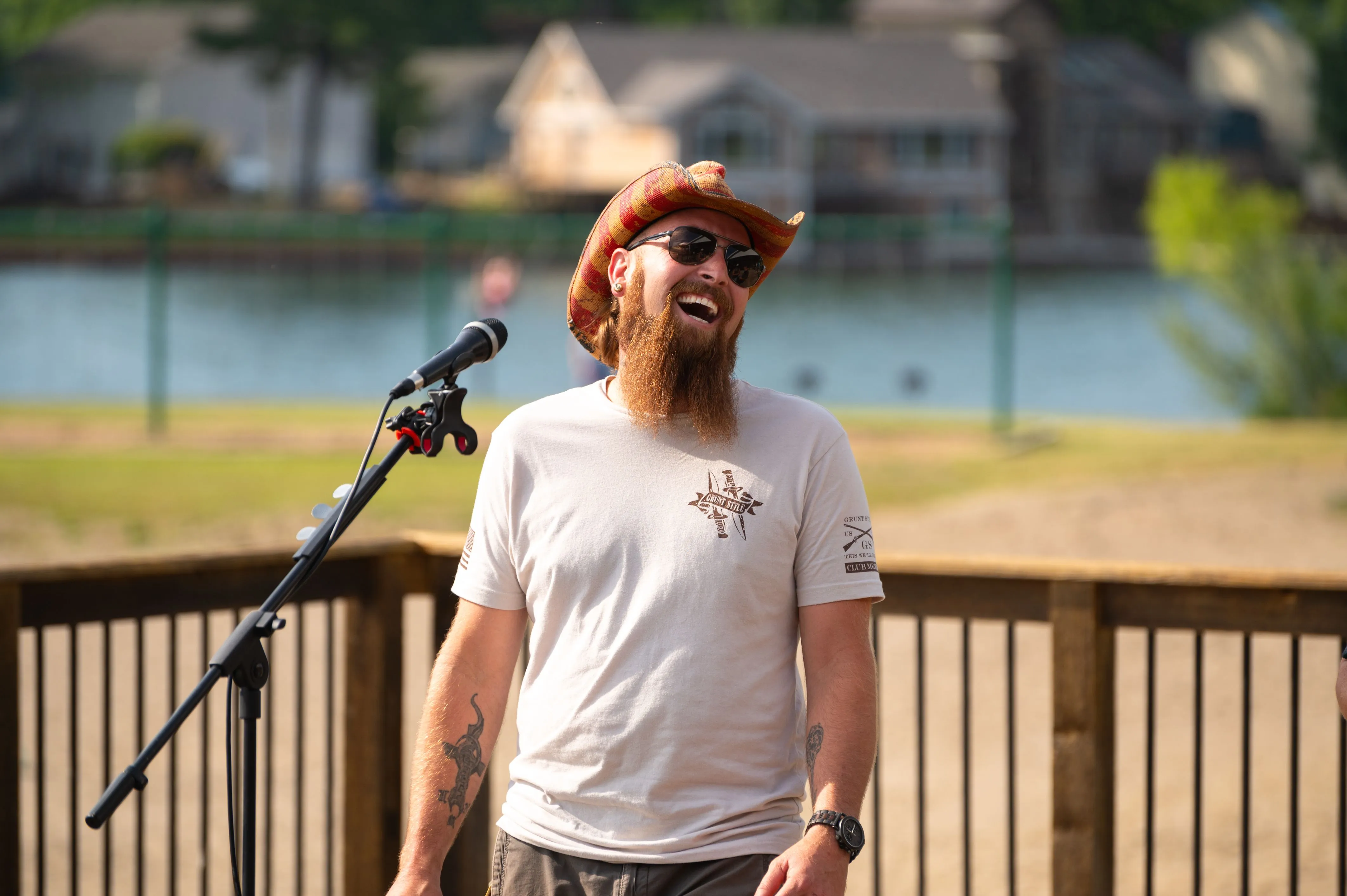 A man with a beard laughing near a microphone stand outdoors.