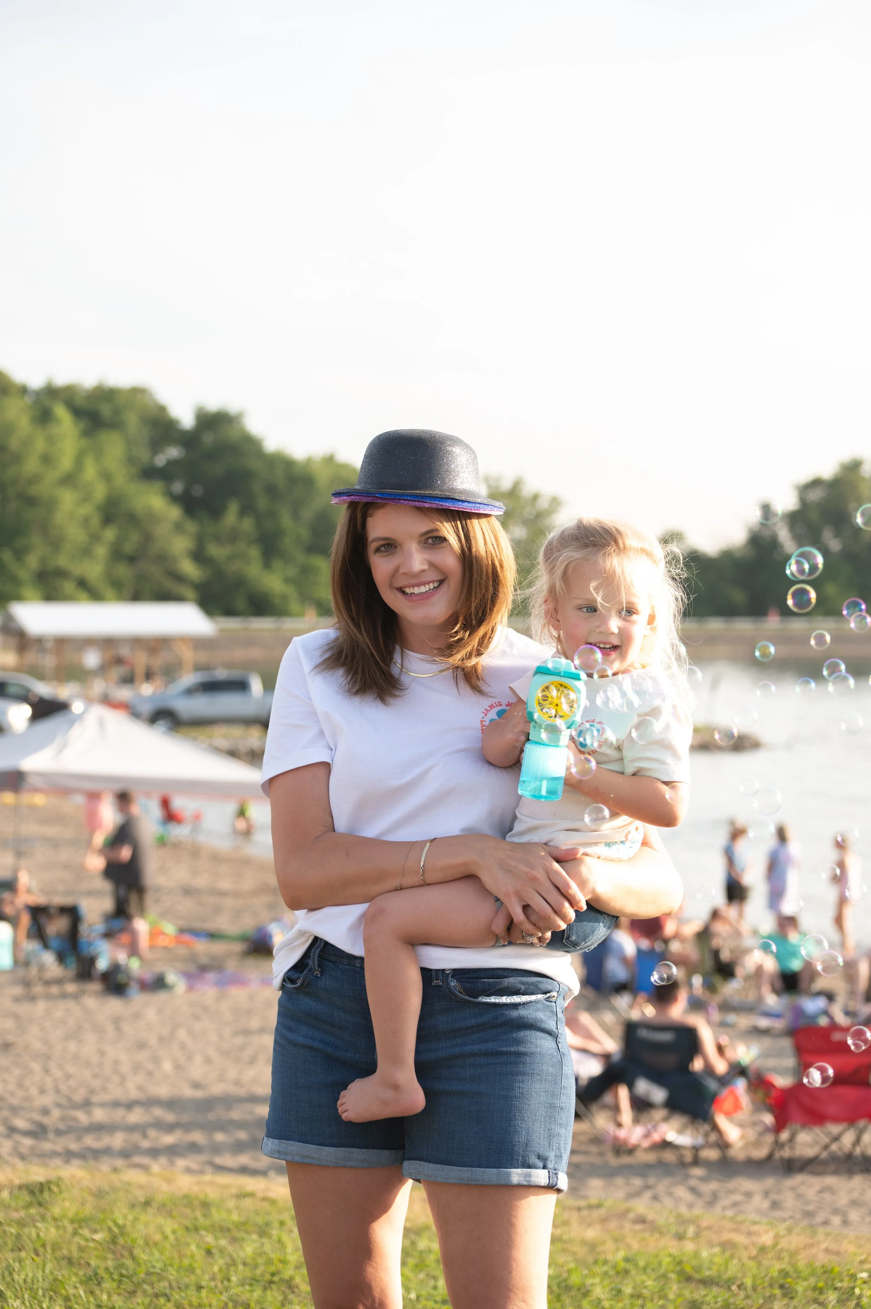 Woman holding a child at a beach with people in the background.