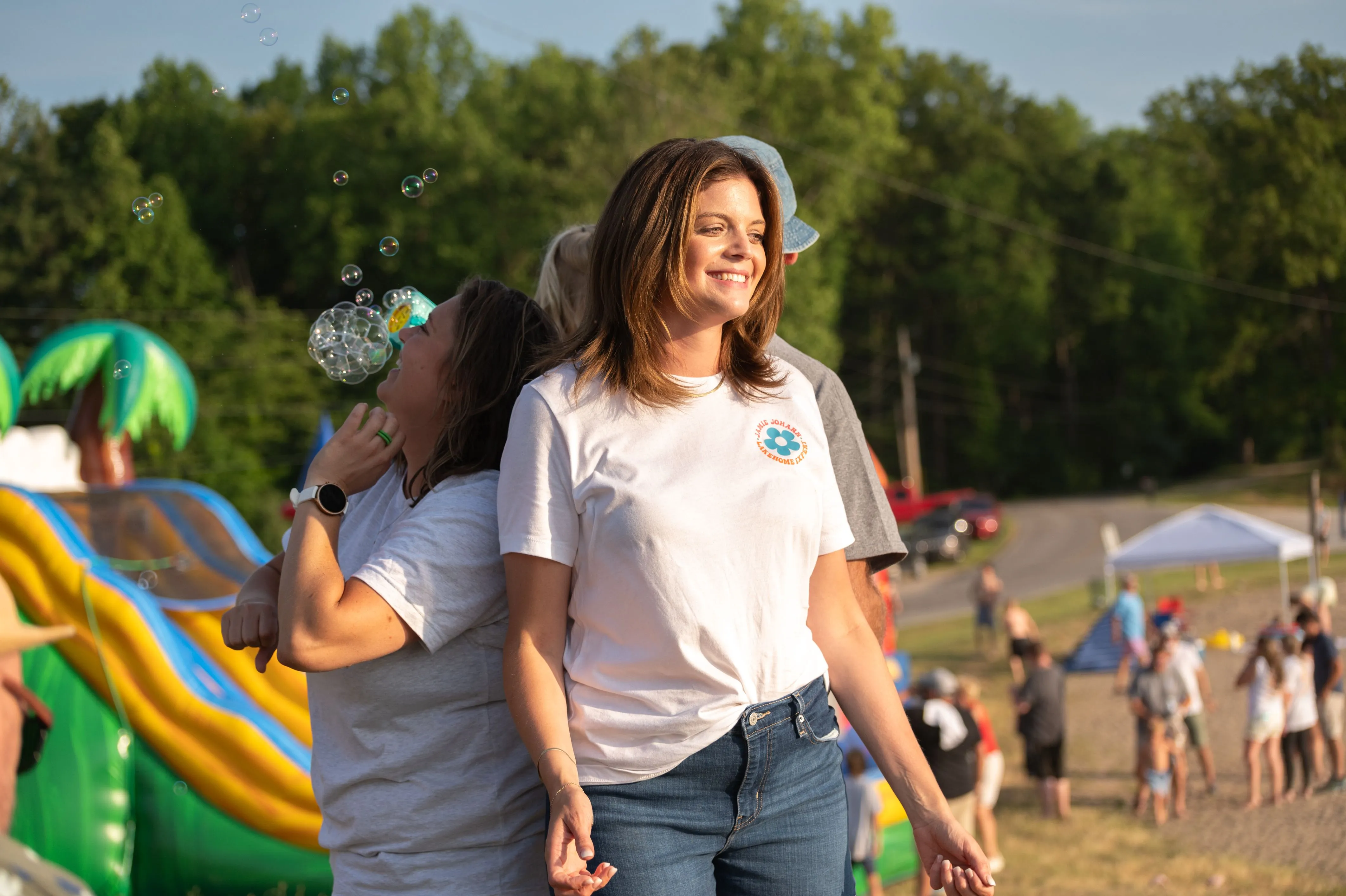 Woman smiling and walking at an outdoor event with people and an inflatable slide in the background.