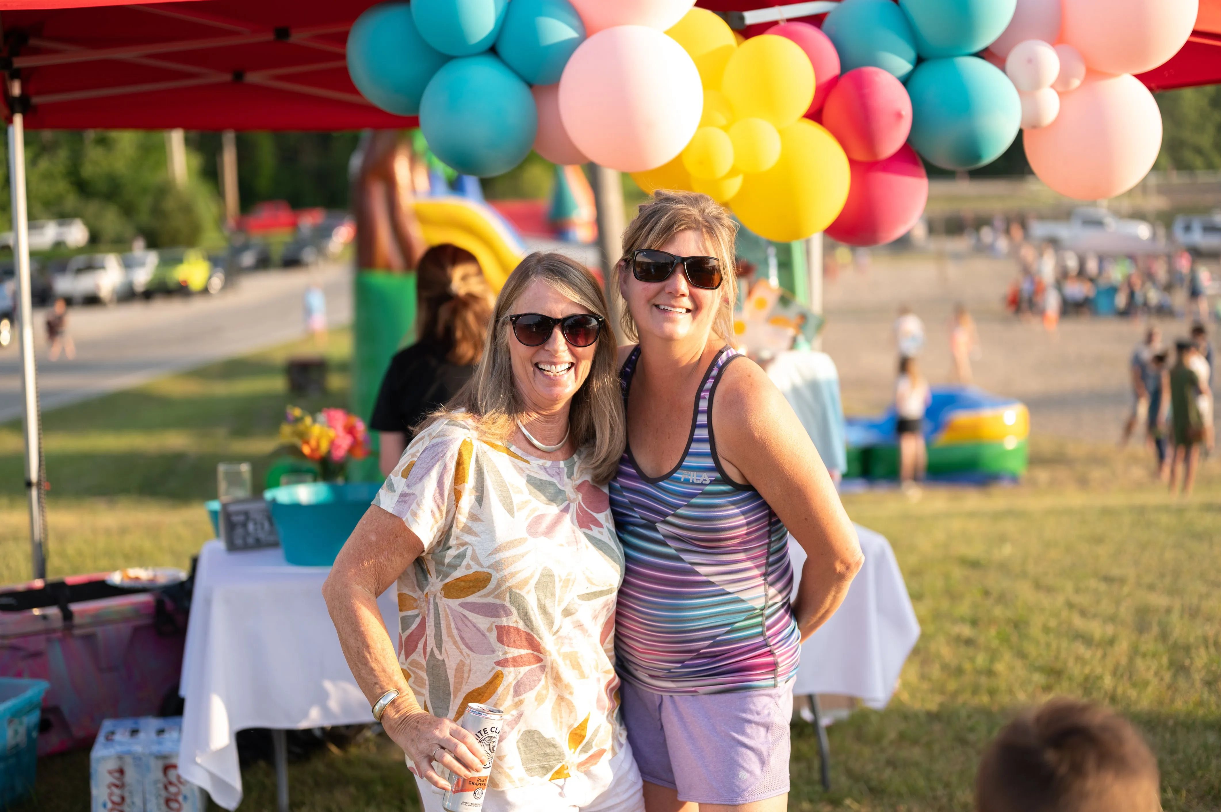 Two women smiling at an outdoor event with colorful balloons in the background.