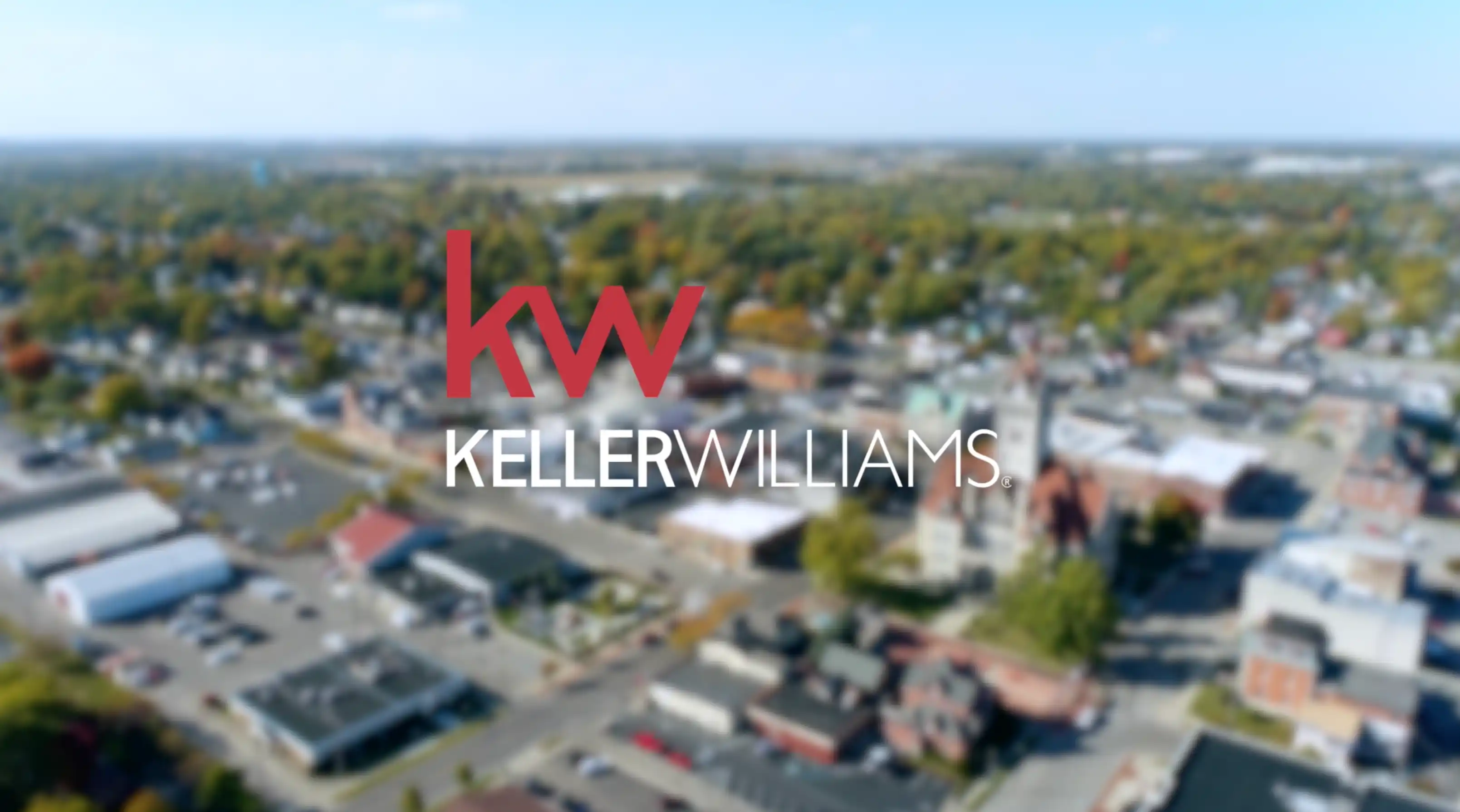 Aerial view of a suburban landscape with buildings and trees, overlaid with the Keller Williams real estate company logo in focus.