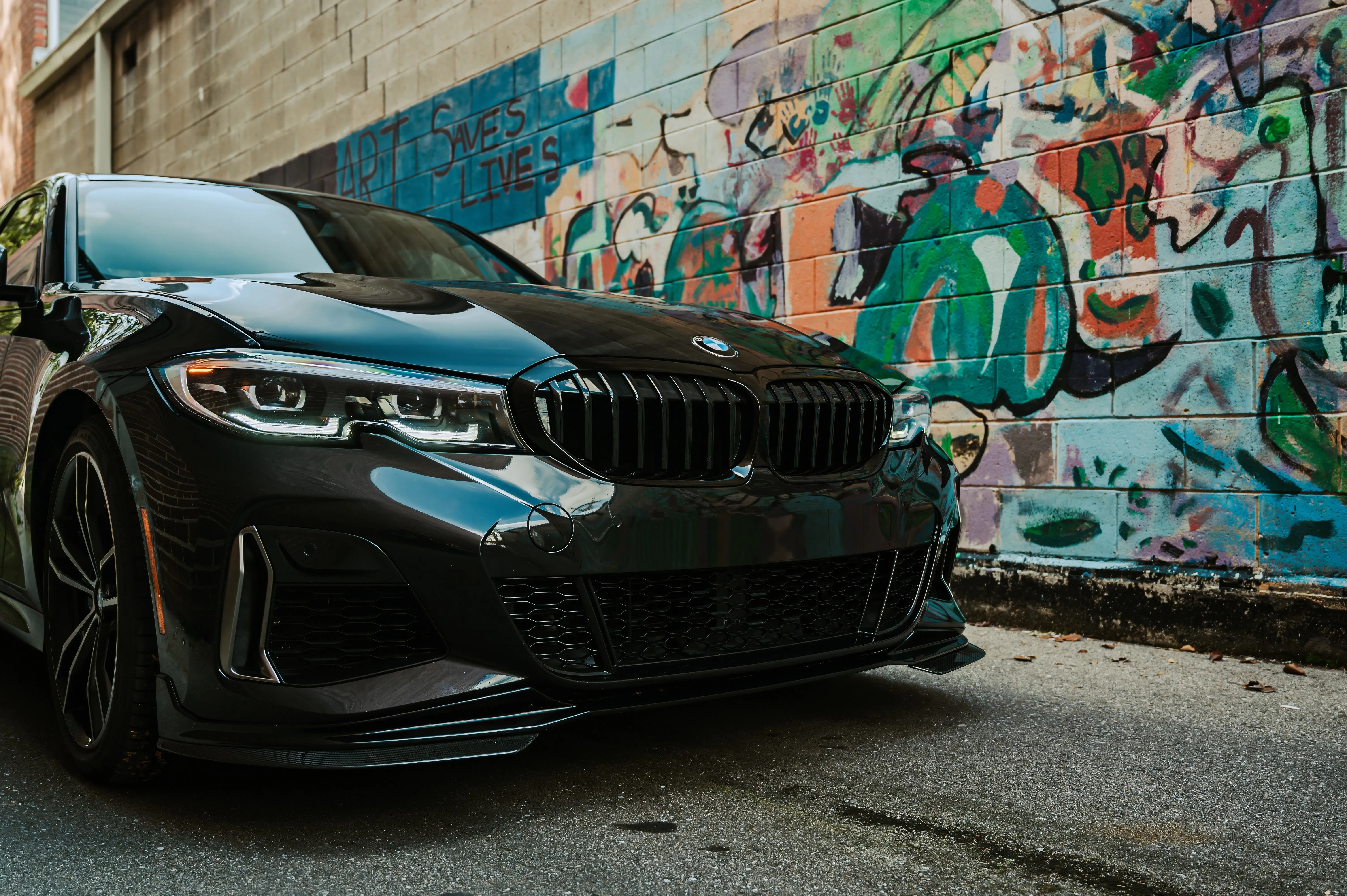 Black BMW car parked in front of a colorful graffiti wall.