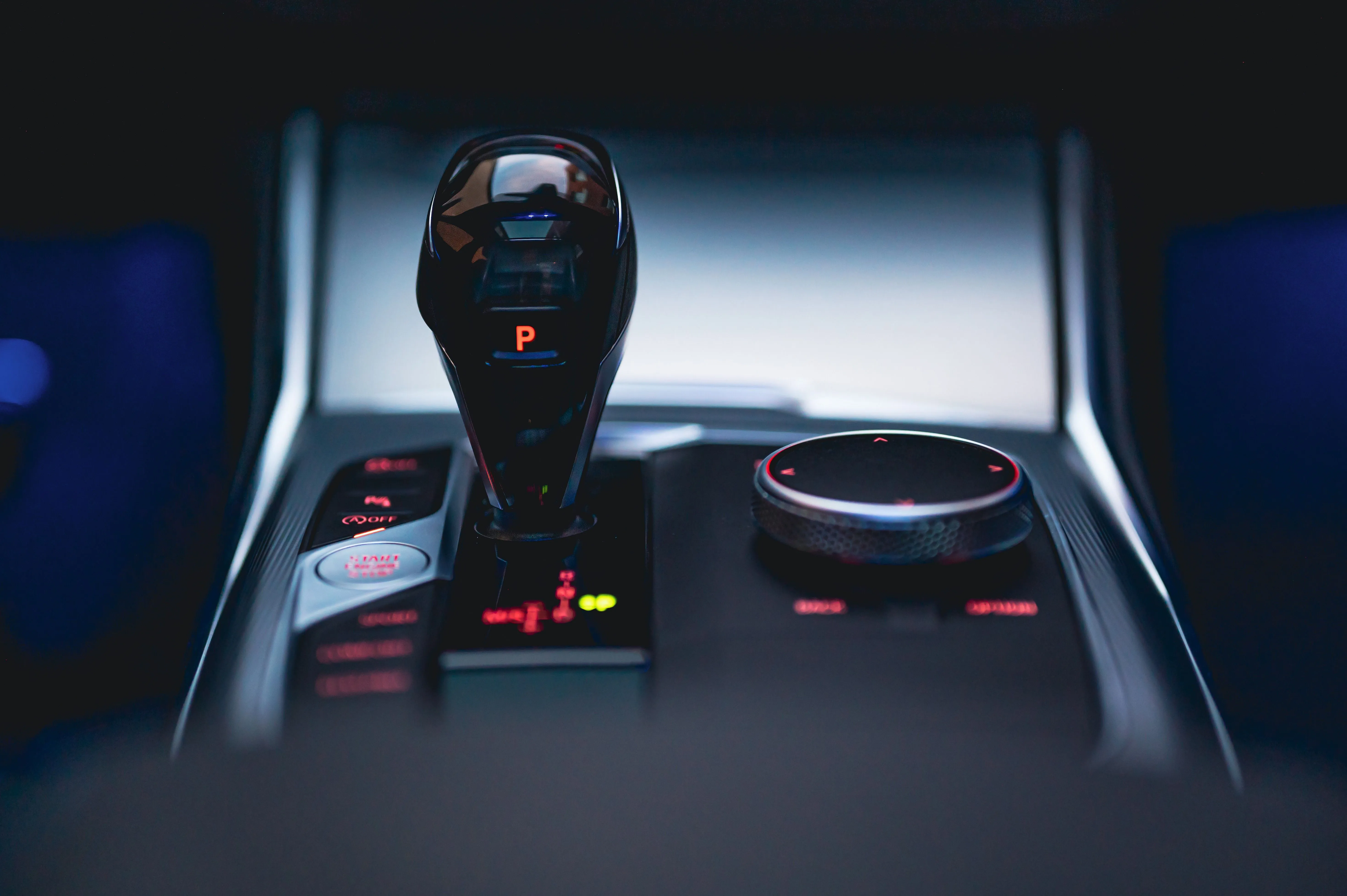 Close-up of an automatic gear stick and vehicle console in blue ambient lighting.