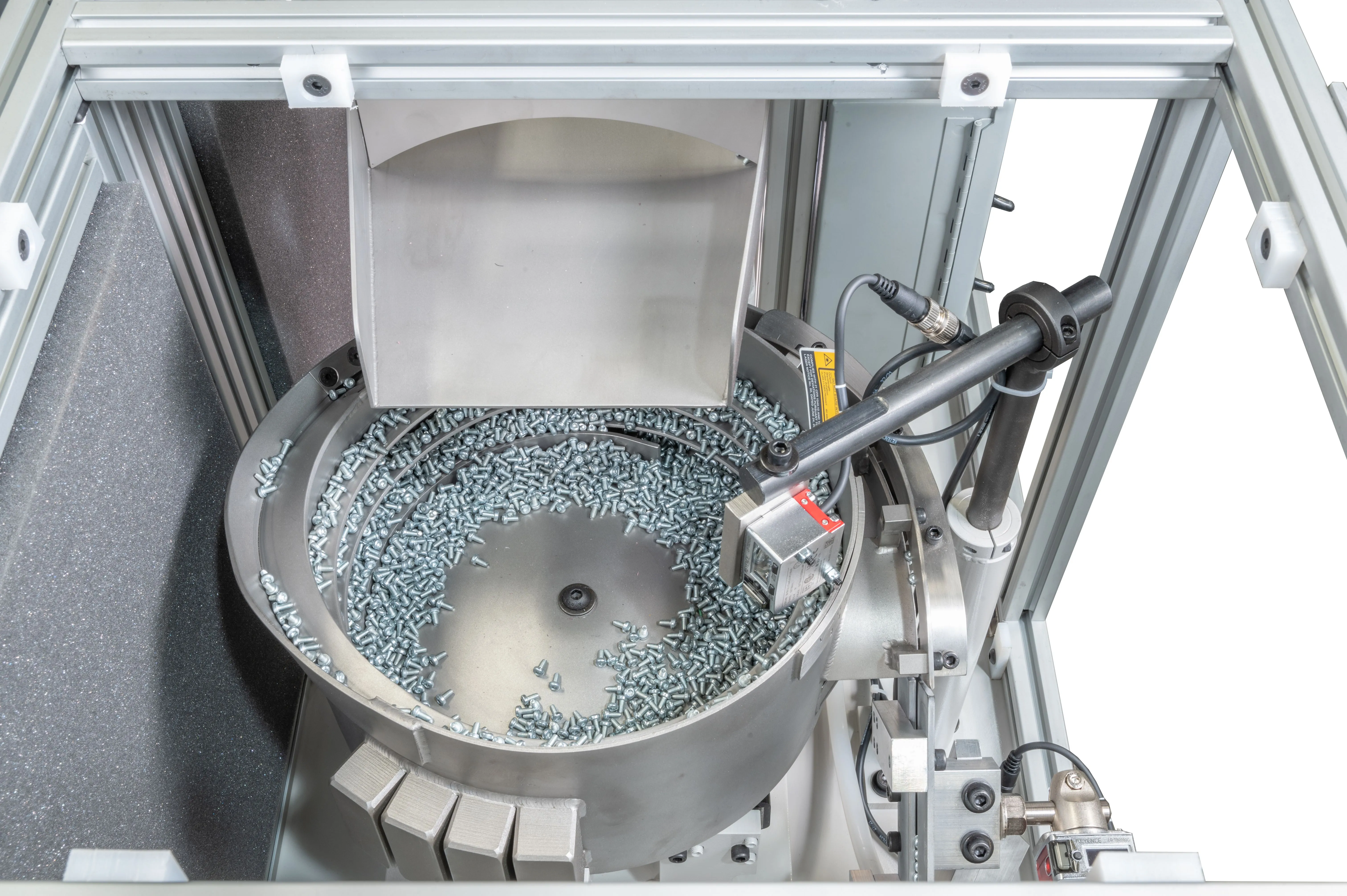 Top view of an industrial vibratory bowl feeder filled with metal fasteners for automated assembly line.