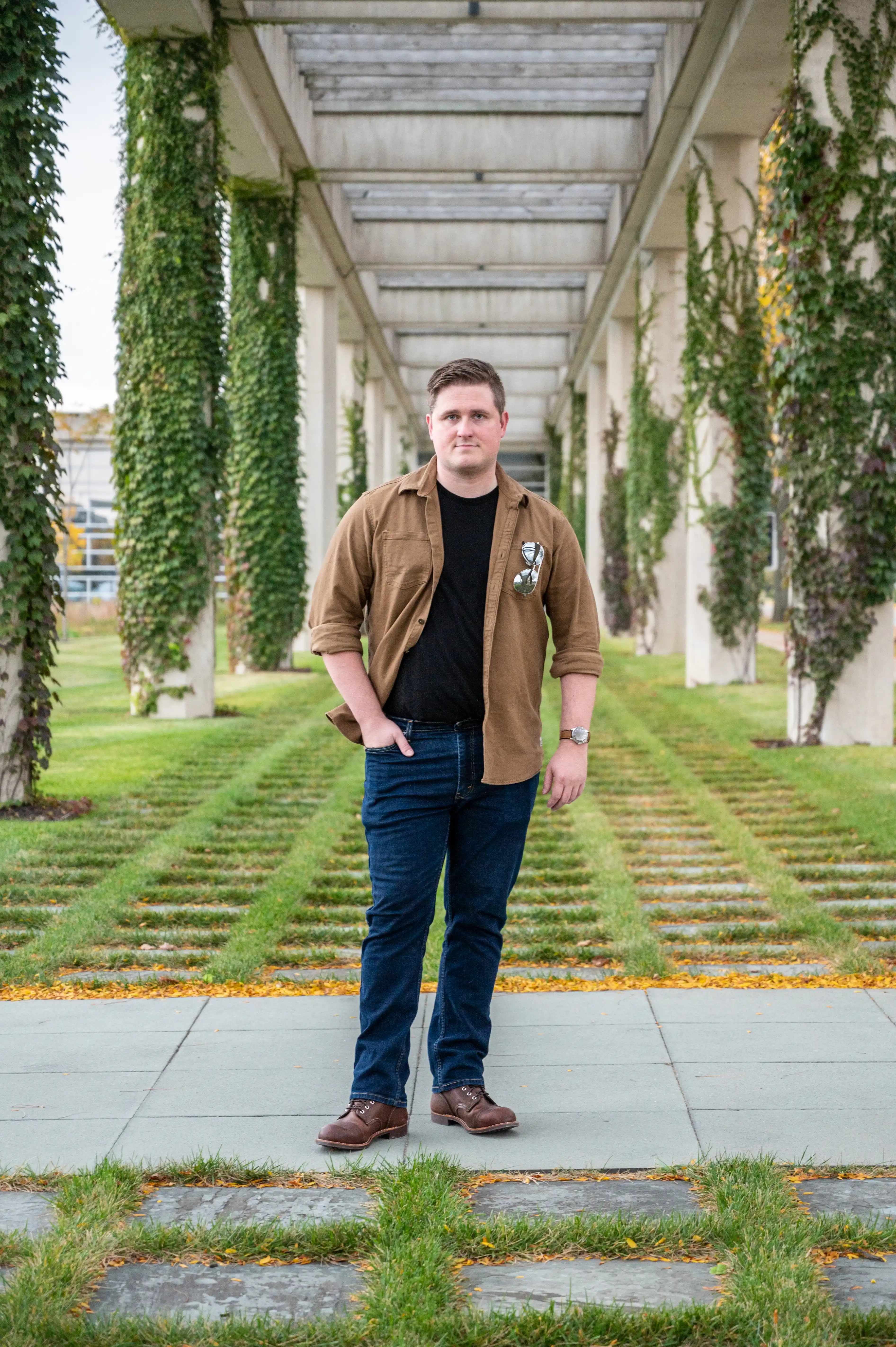 Man standing on a pathway with greenery and vines on columns in the background.