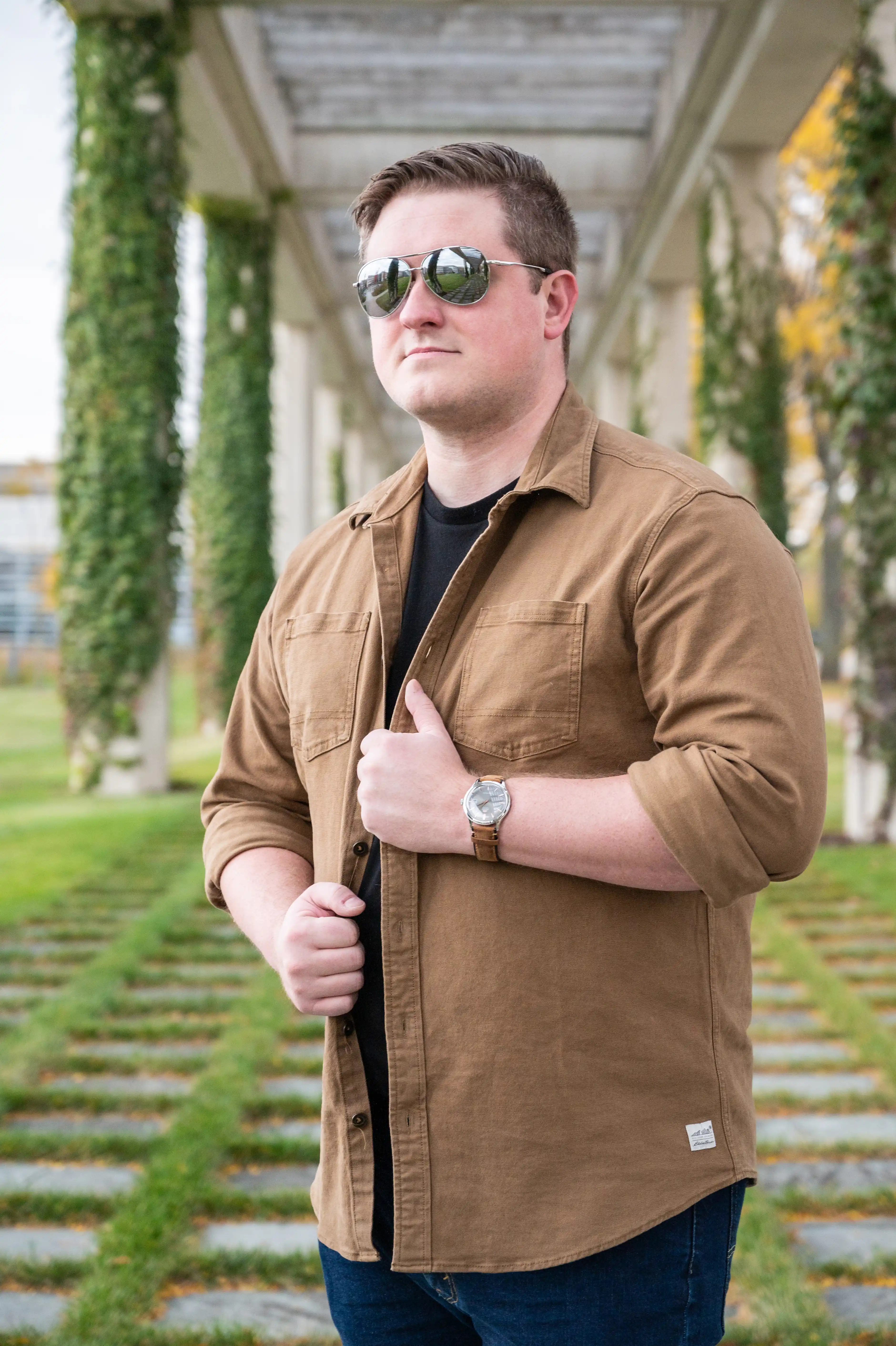 Man in sunglasses standing under a pergola with hanging greenery.