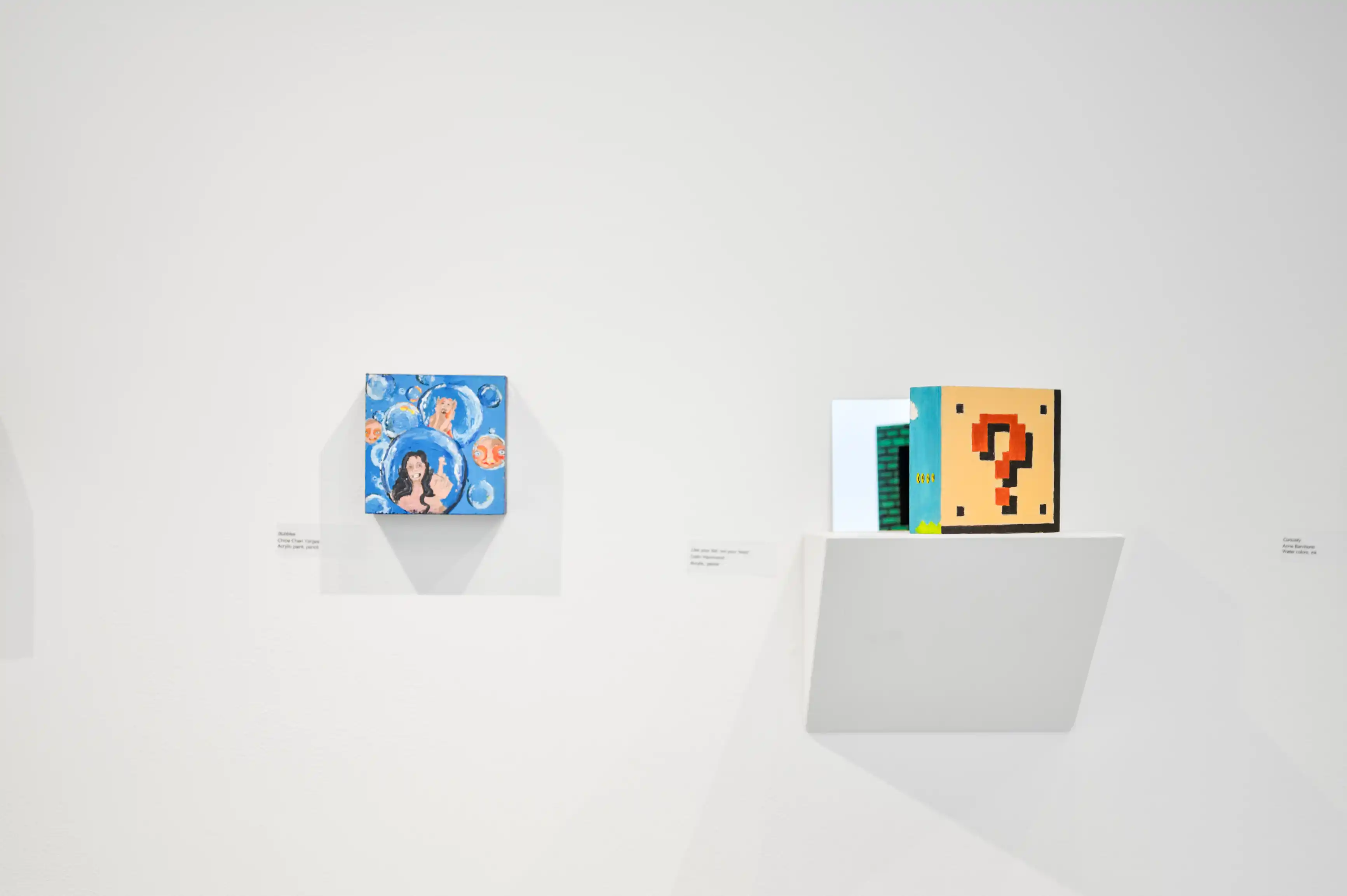 Art gallery wall displaying two colorful paintings, one featuring an abstract blue and orange design resembling a question mark, and another with a figurative depiction amidst blue swirls and orange spheres.