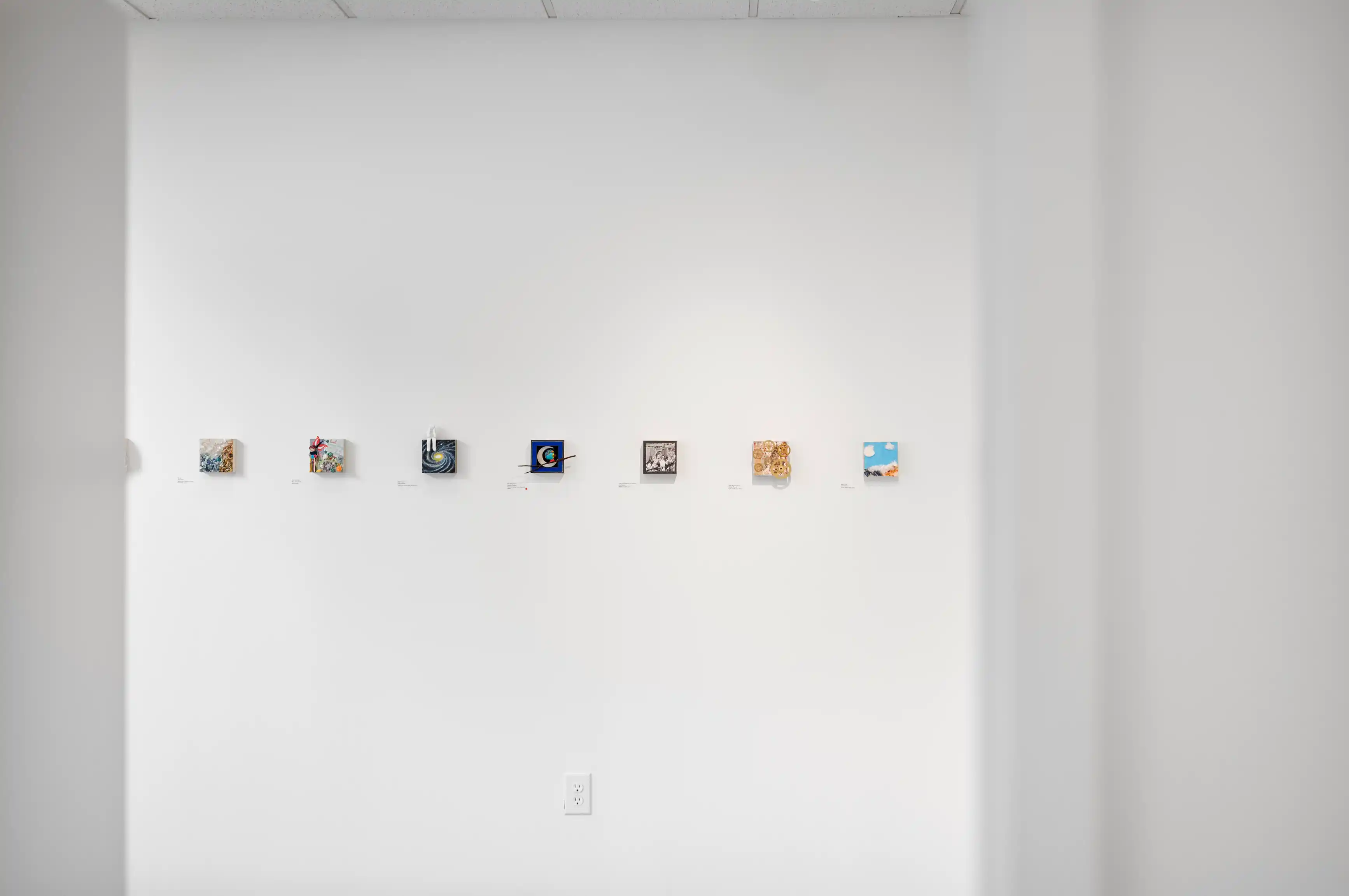 A bright interior wall displaying a variety of small, framed abstract artworks evenly spaced in a horizontal line.