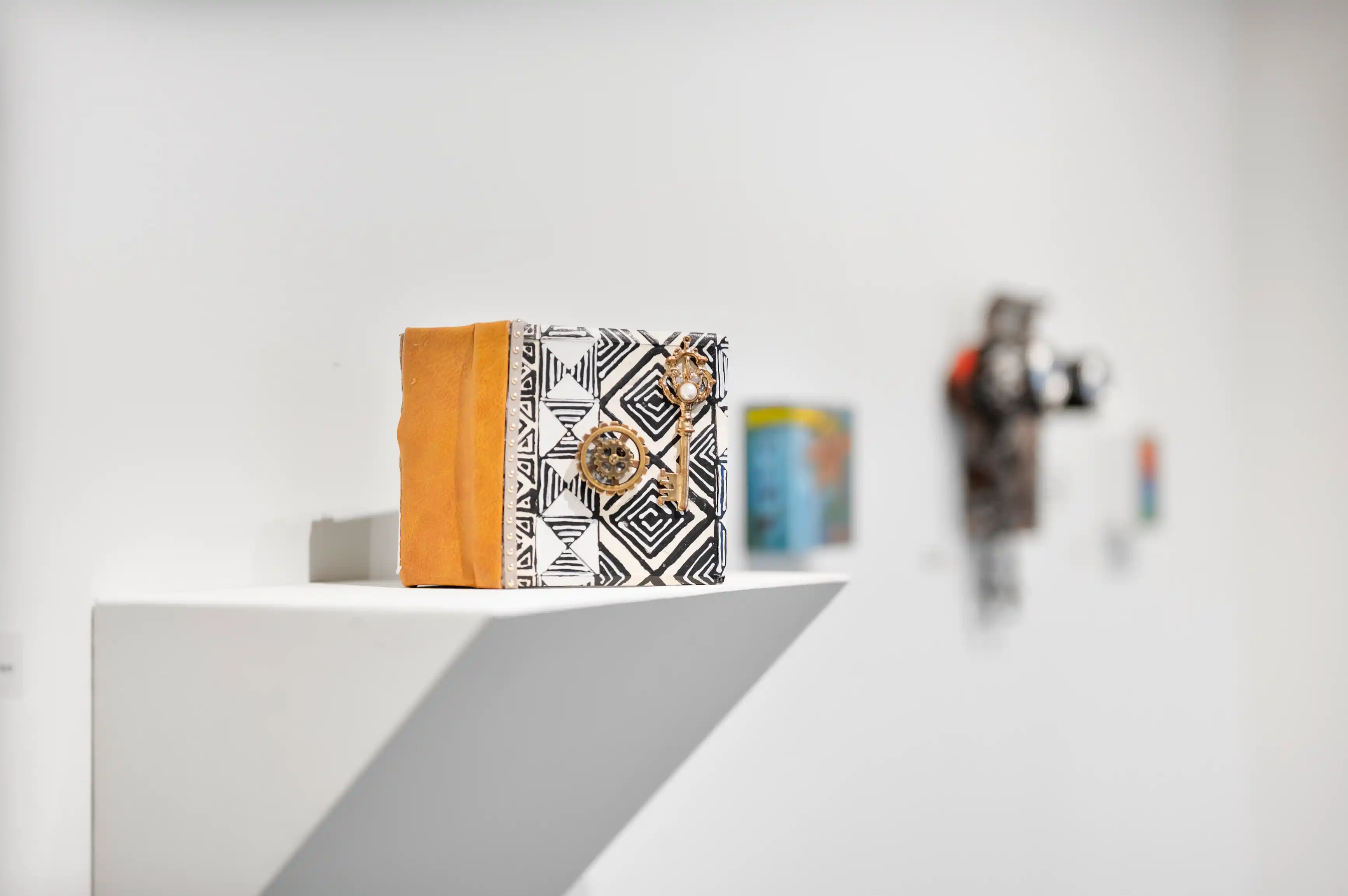 Art installation with a patterned box and blurry background featuring gallery pieces.