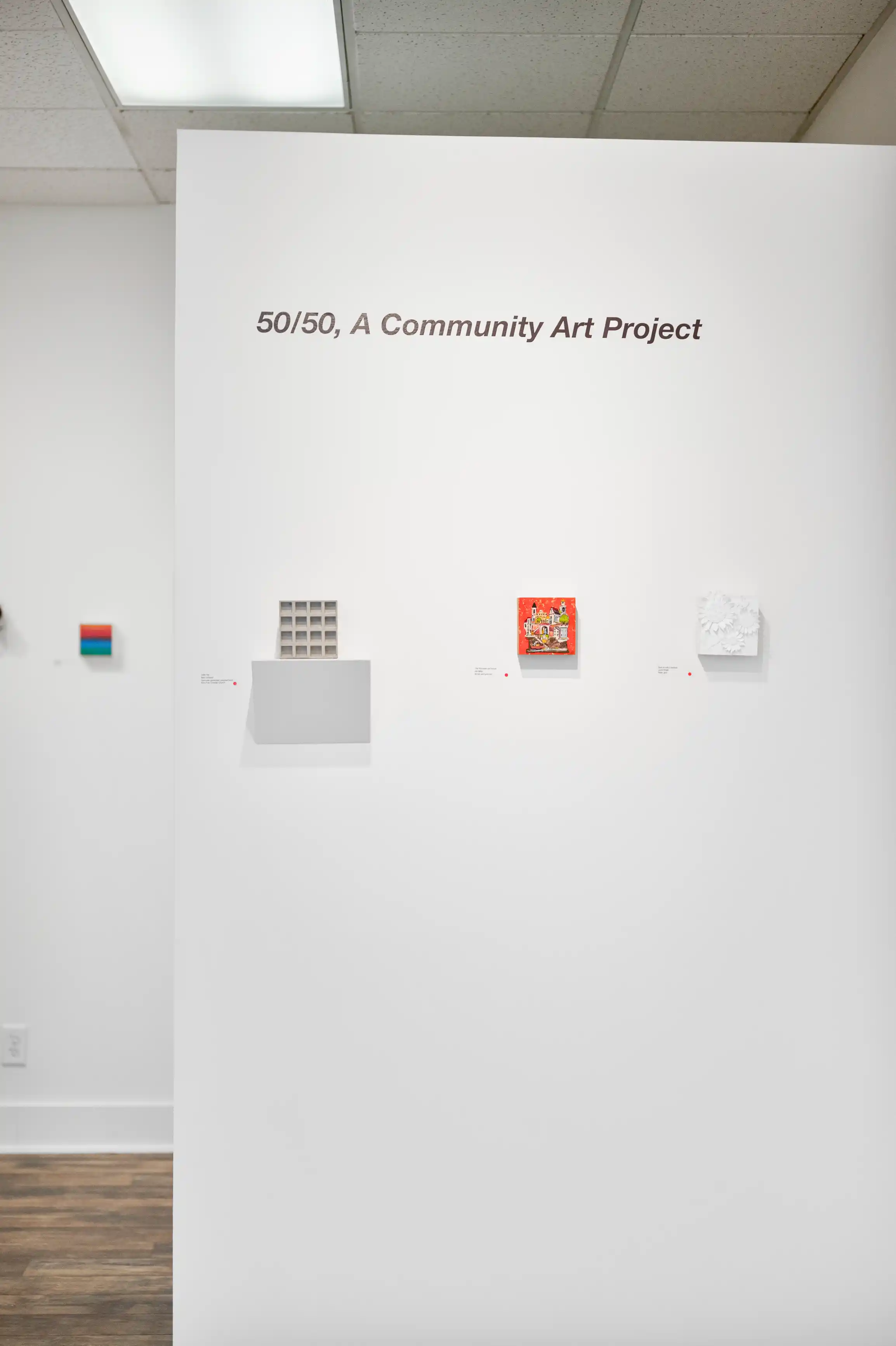 Interior of an art gallery featuring the "50/50, A Community Art Project" with various small artworks displayed on a white wall.