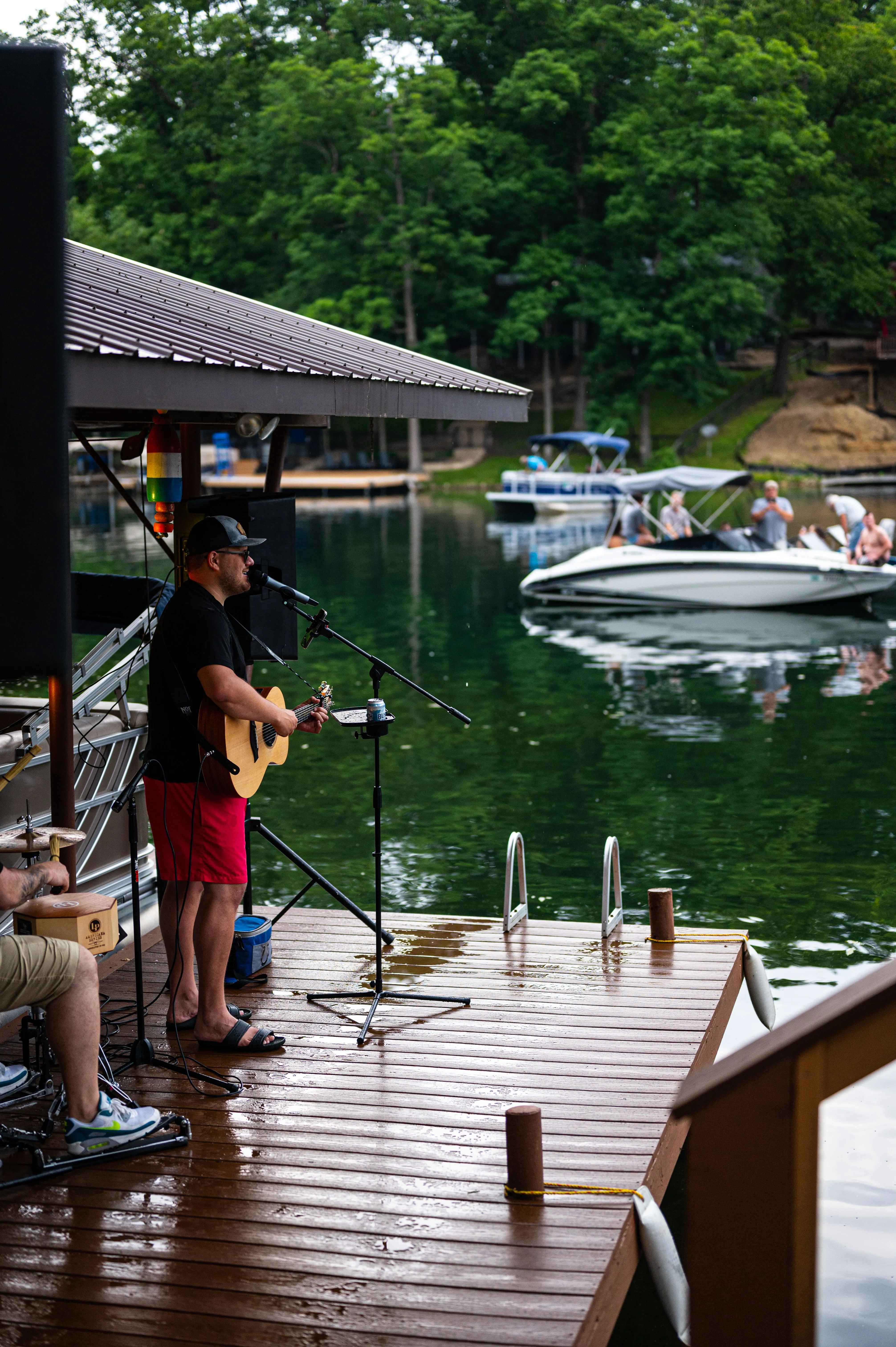 Musician playing guitar on a dock by the lake with boats in the background.