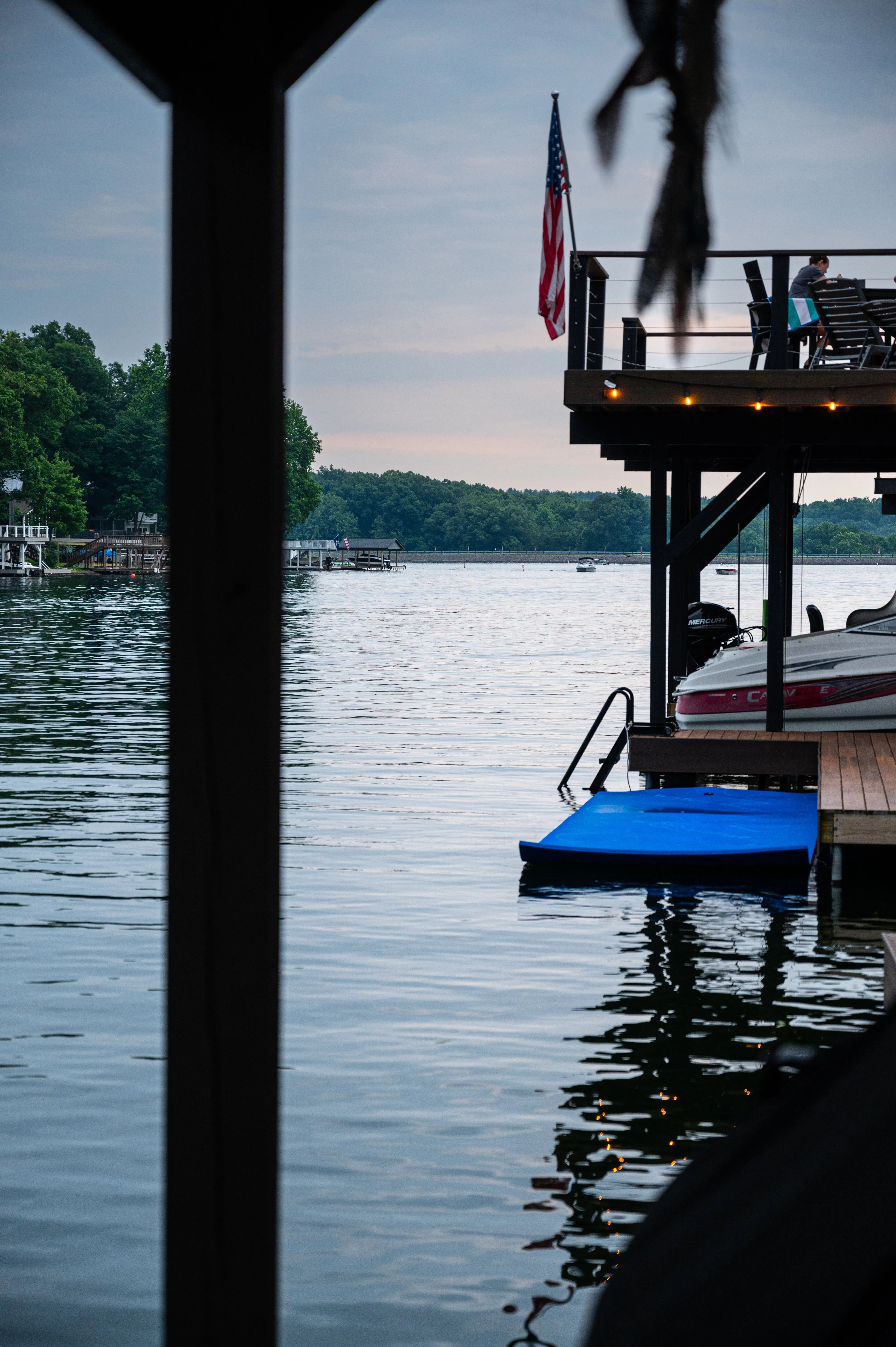 Tranquil lake view with a dock, a fluttering American flag, and a diving platform in the early evening.