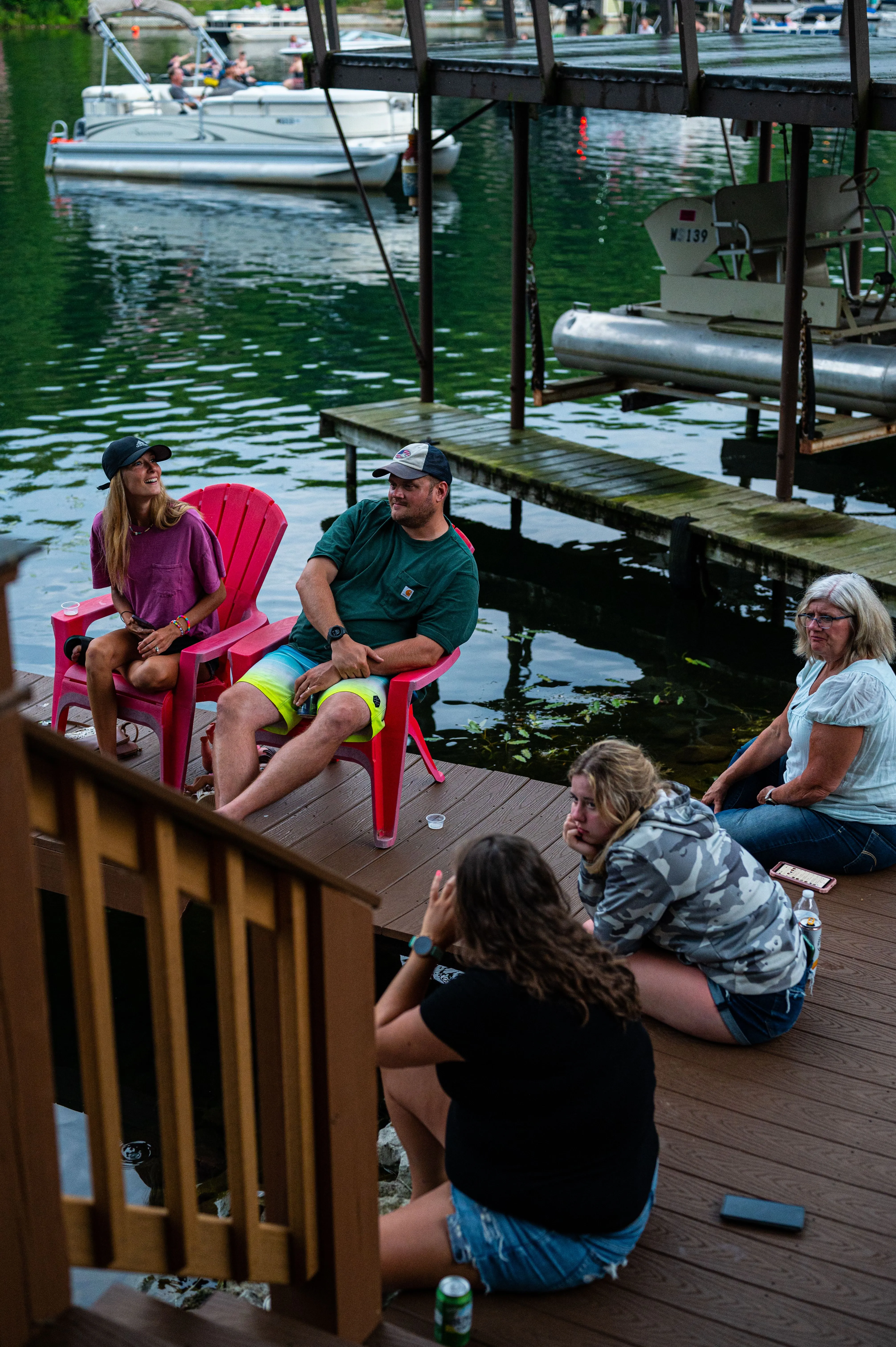 Group of people sitting and chatting on a lakeside deck with boats docked in the background