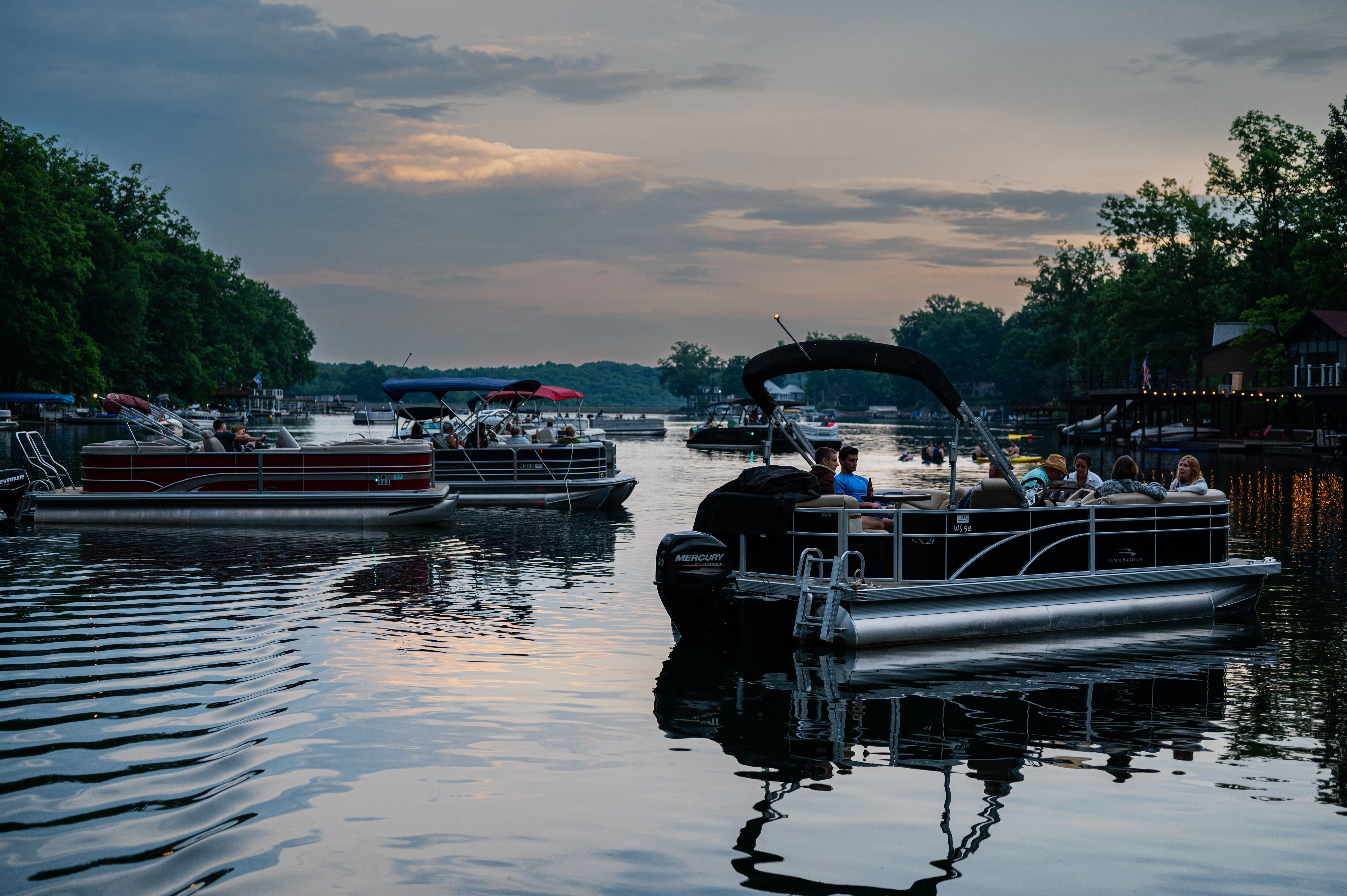 Pontoons and boats moored on a calm river at twilight with trees and a hint of sunset in the background.