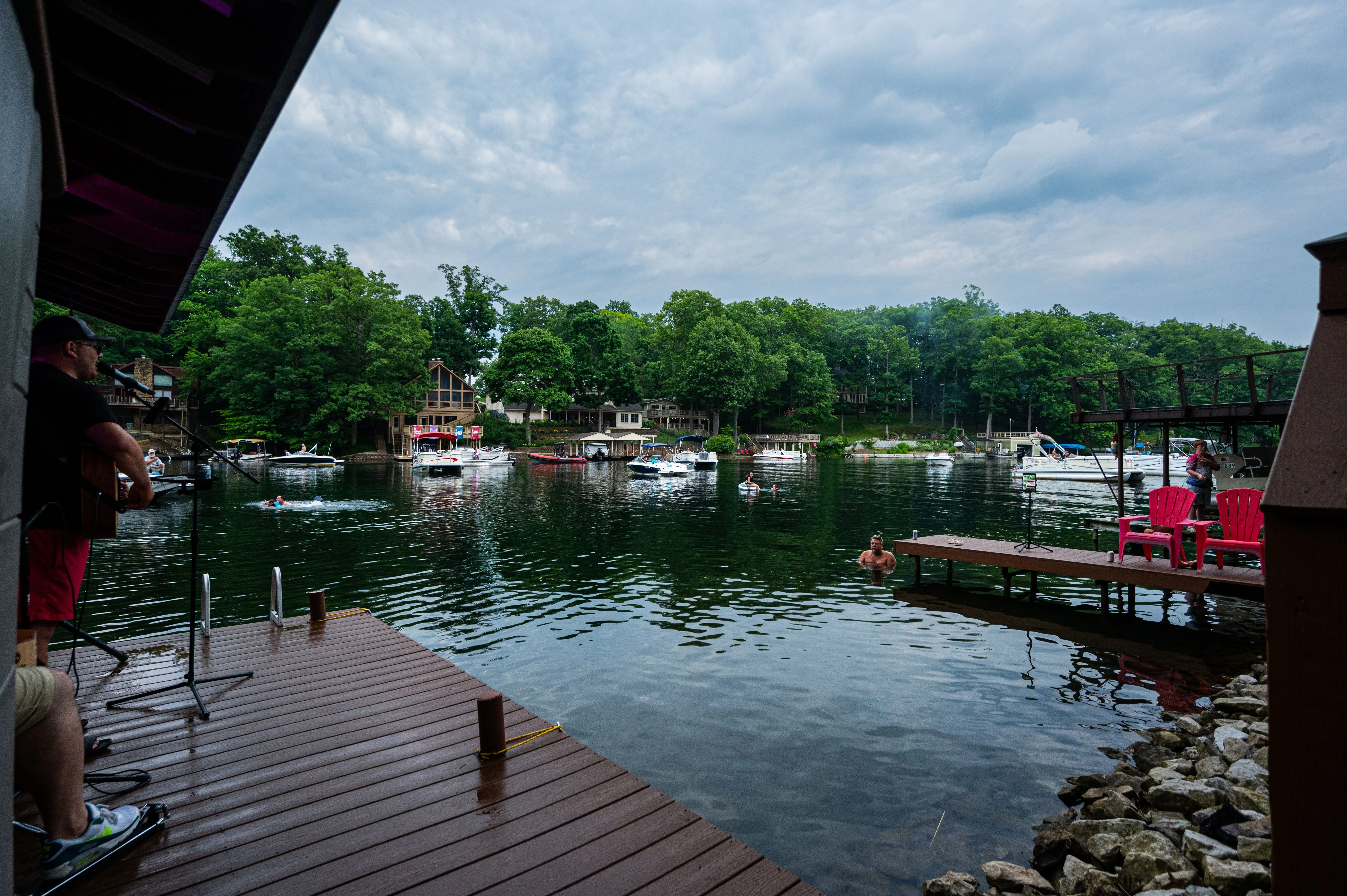 View from a lakeside dock with moored boats, outdoor seating, and overcast skies.