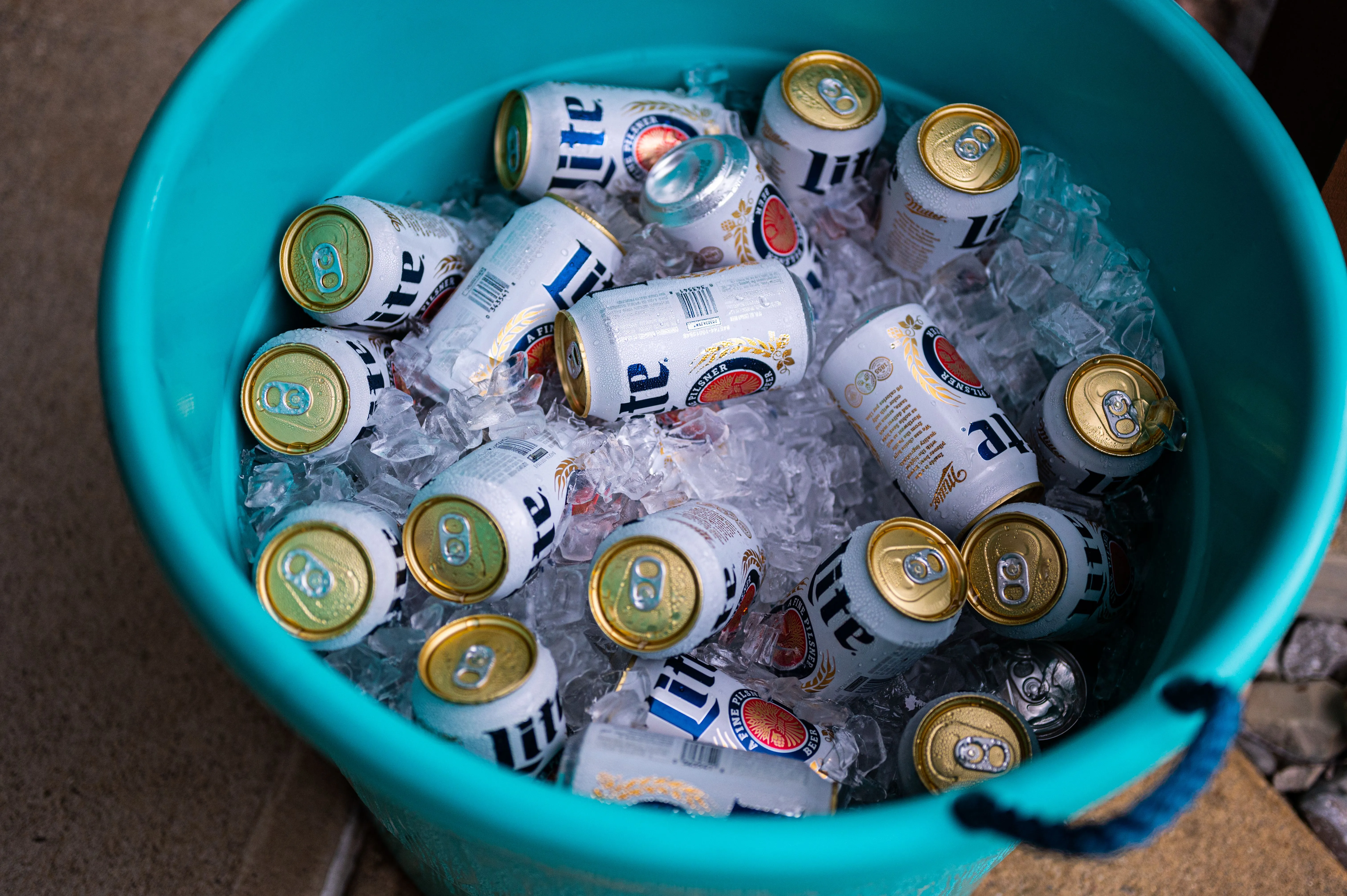 A blue bucket filled with ice and assorted cans of beer.