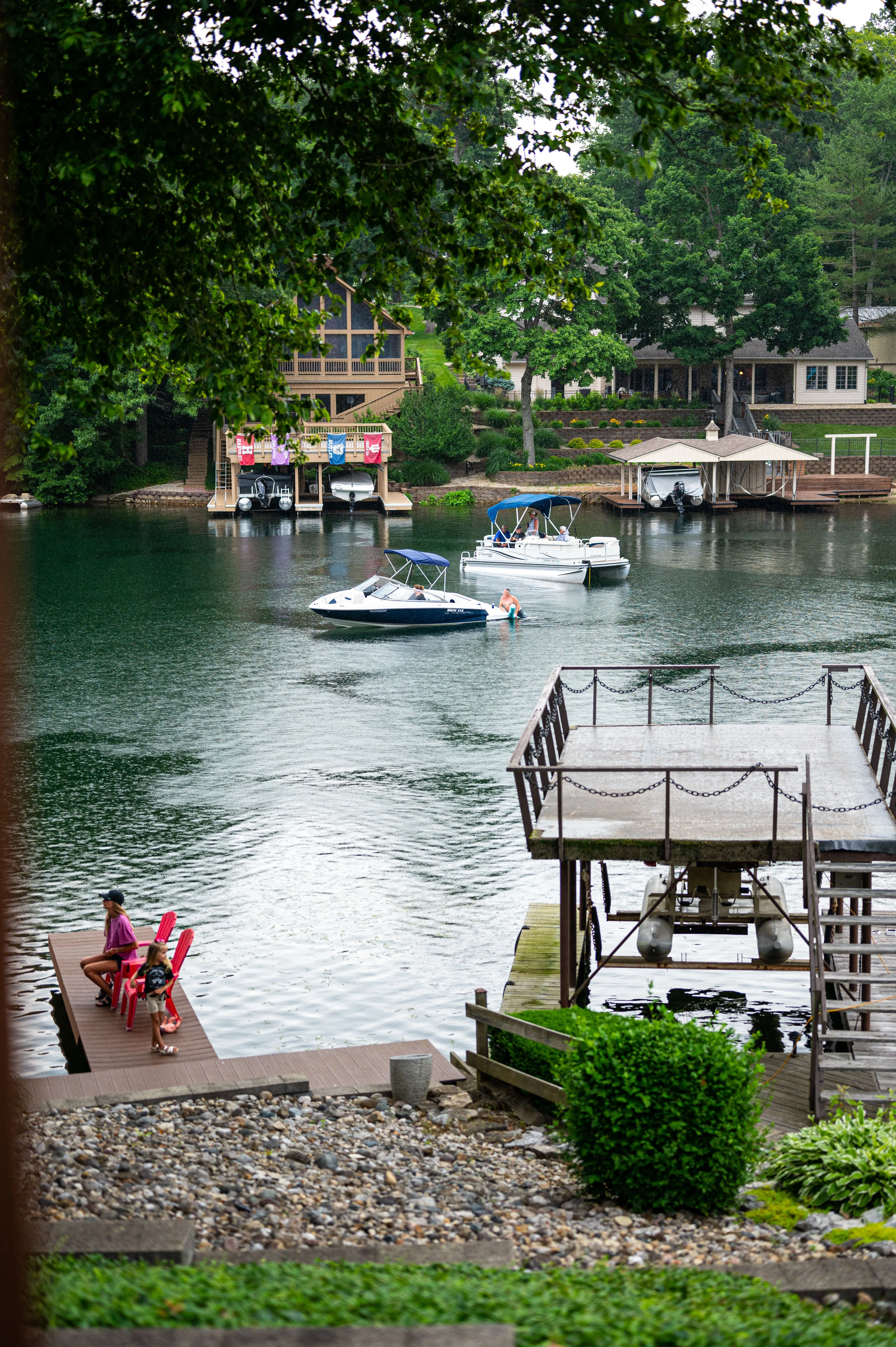 Serene lakeside scene with a boat in the distance, surrounded by greenery and residential buildings, with a wooden staircase leading to the water's edge.