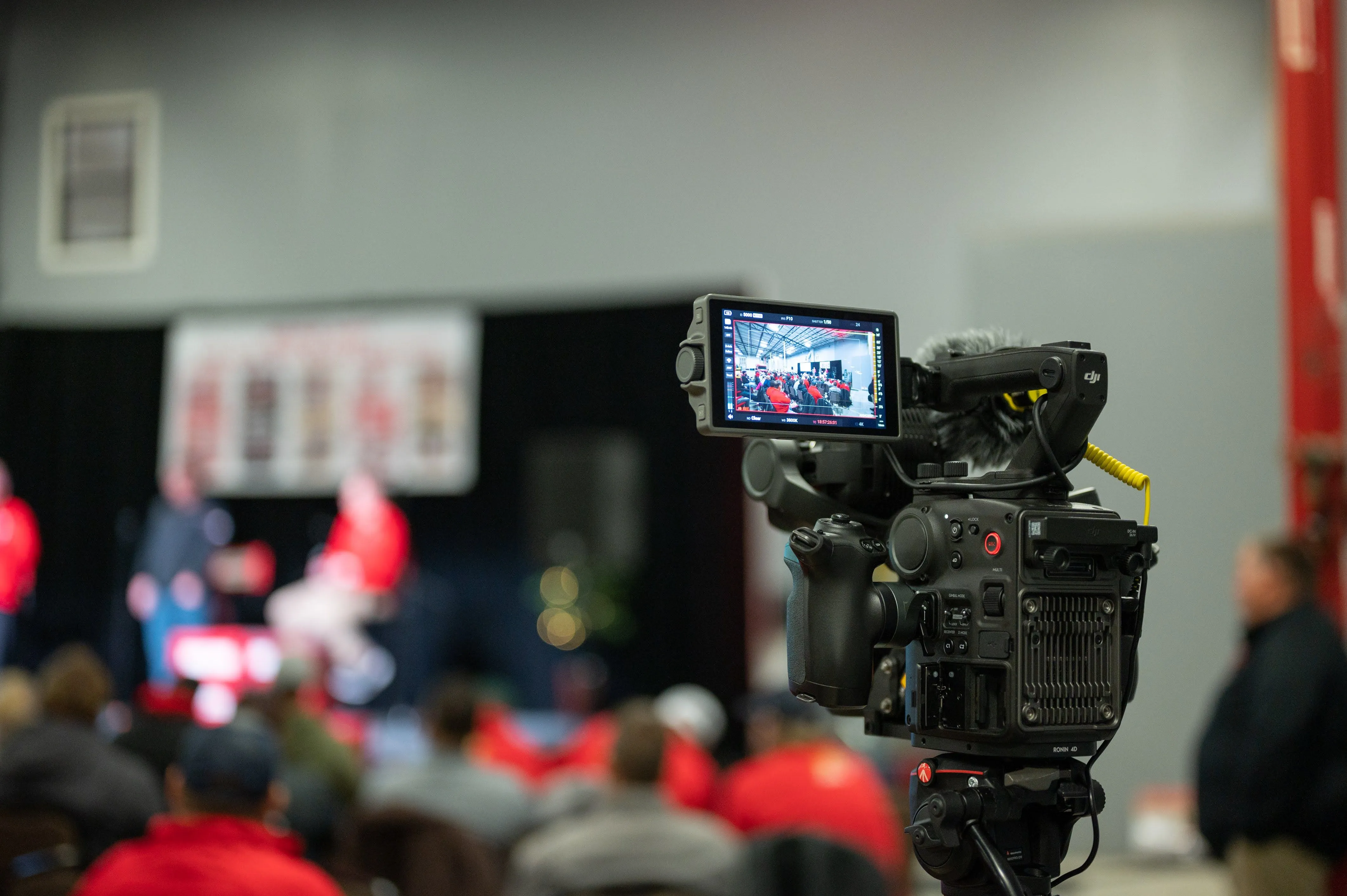 Professional video camera focused in the foreground with a blurred panel discussion being recorded in the background.
