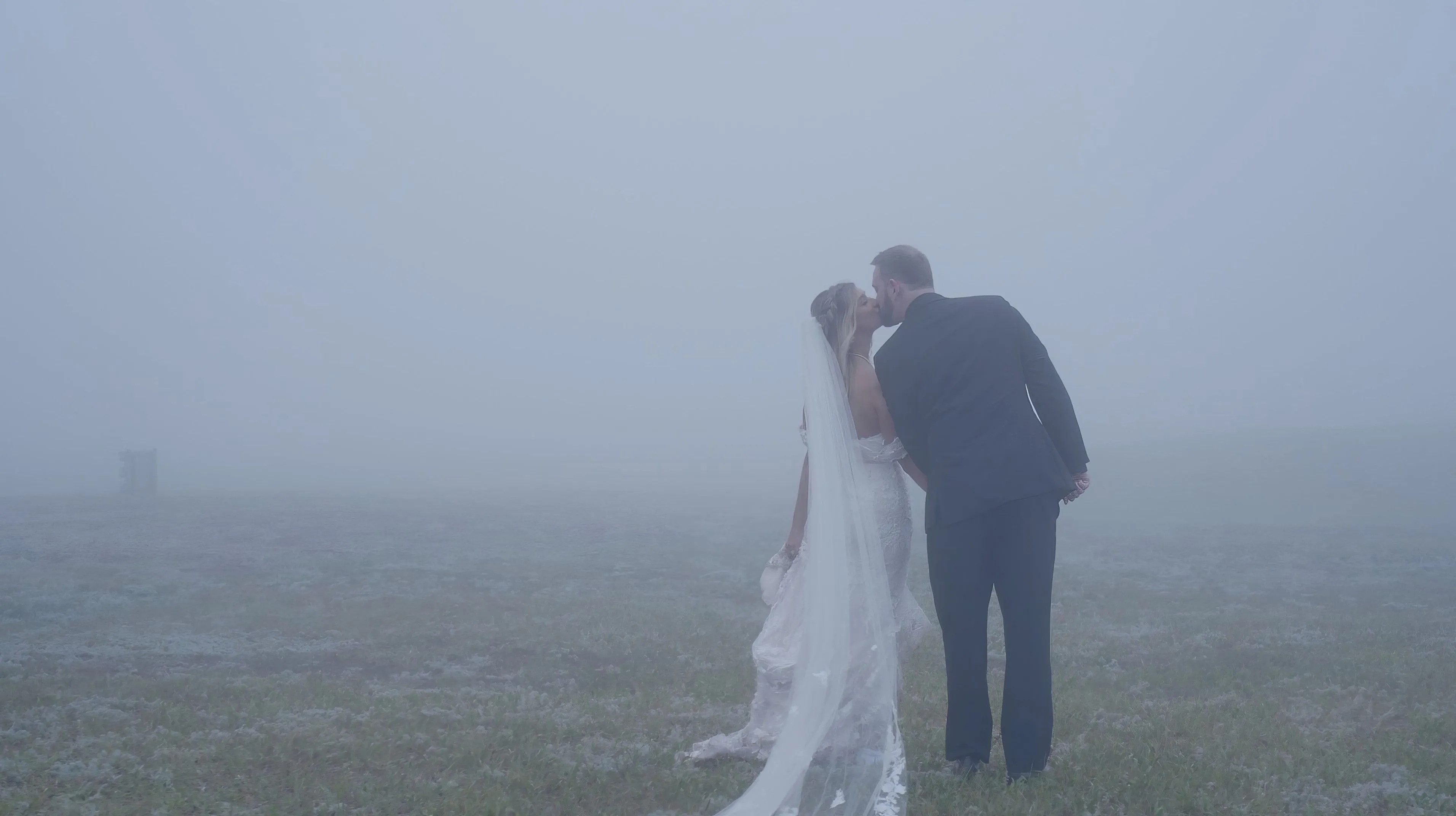 Bride and groom sharing a kiss in a foggy, misty landscape.