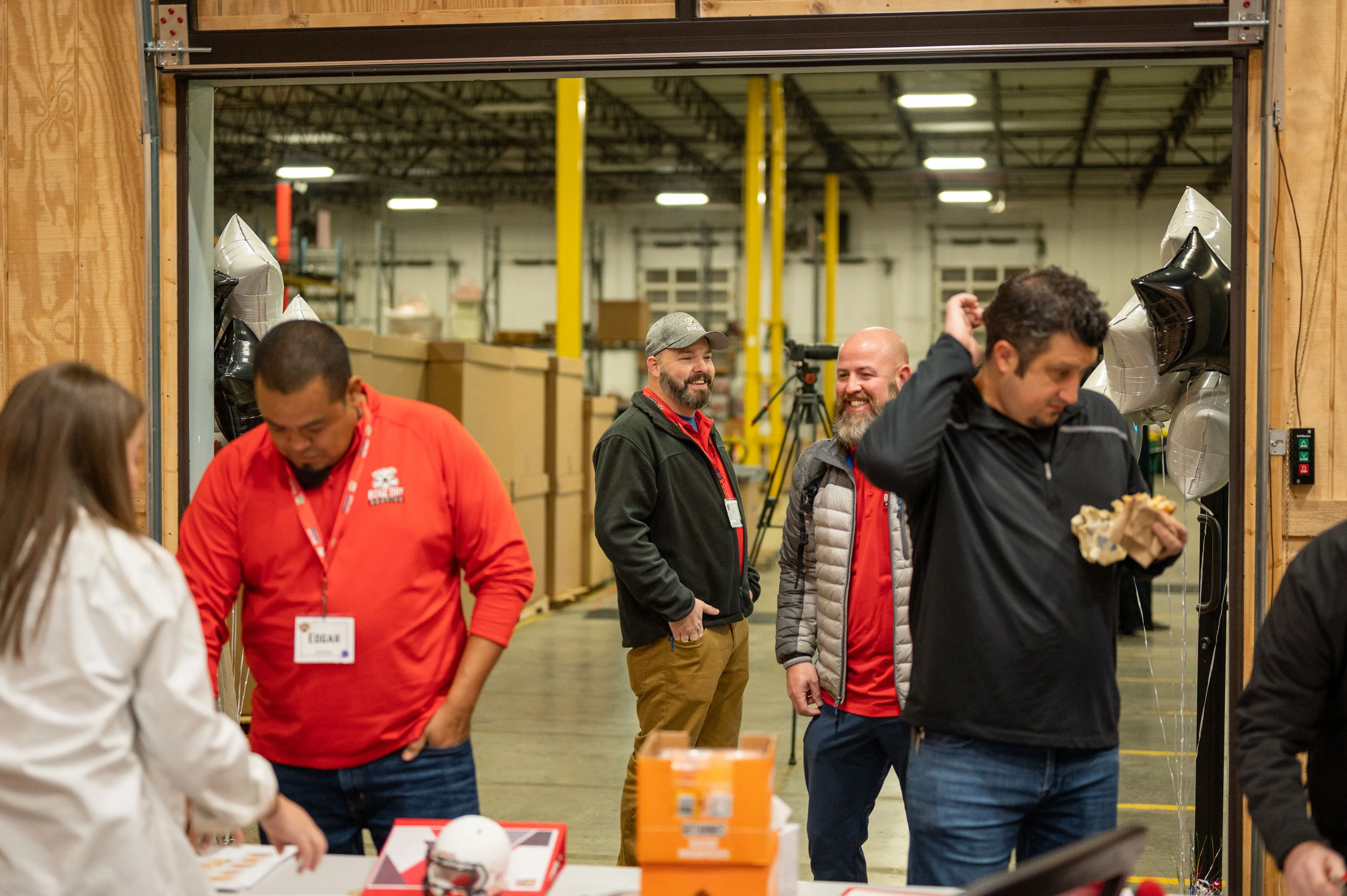 Group of people engaged in an activity in a warehouse setting, with some individuals wearing name tags and carrying items.