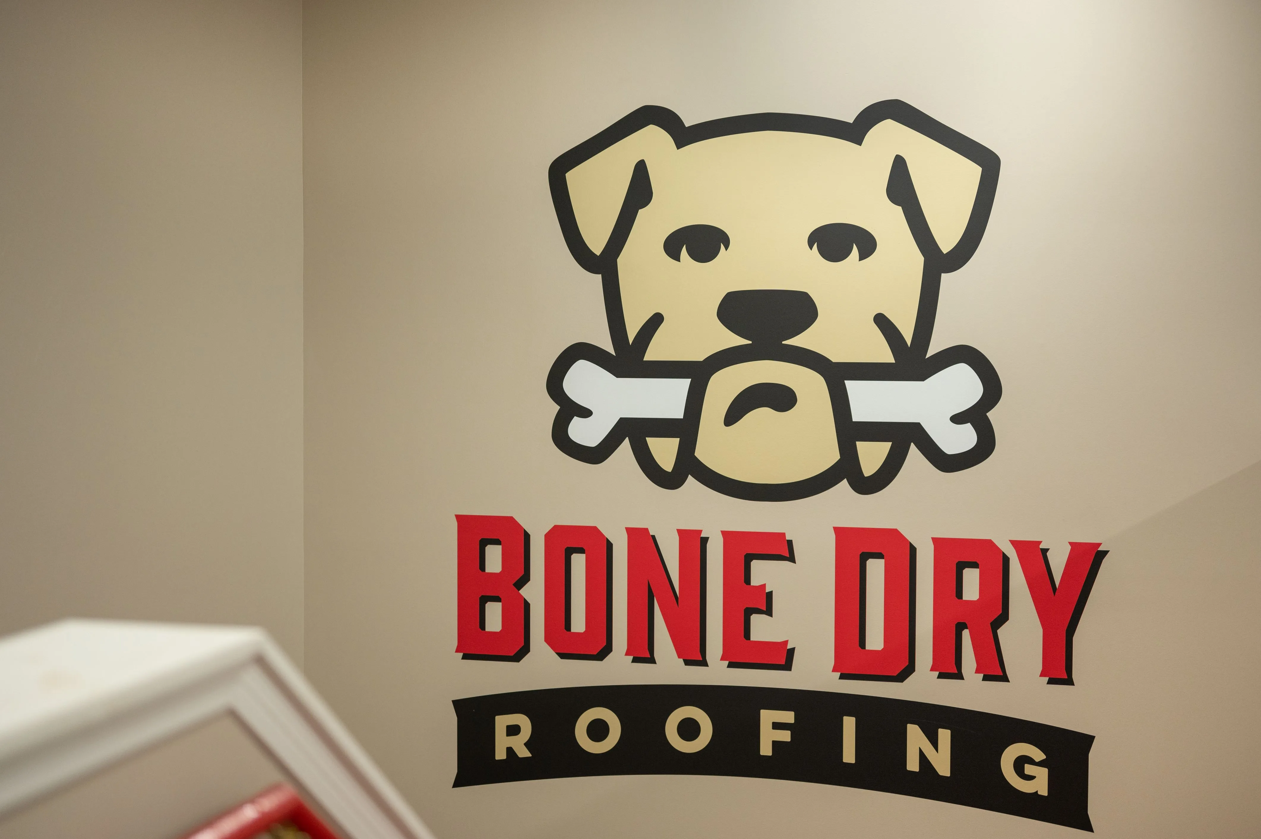 Logo of Bone Dry Roofing featuring a cartoon dog holding a bone in its mouth with stylized text.