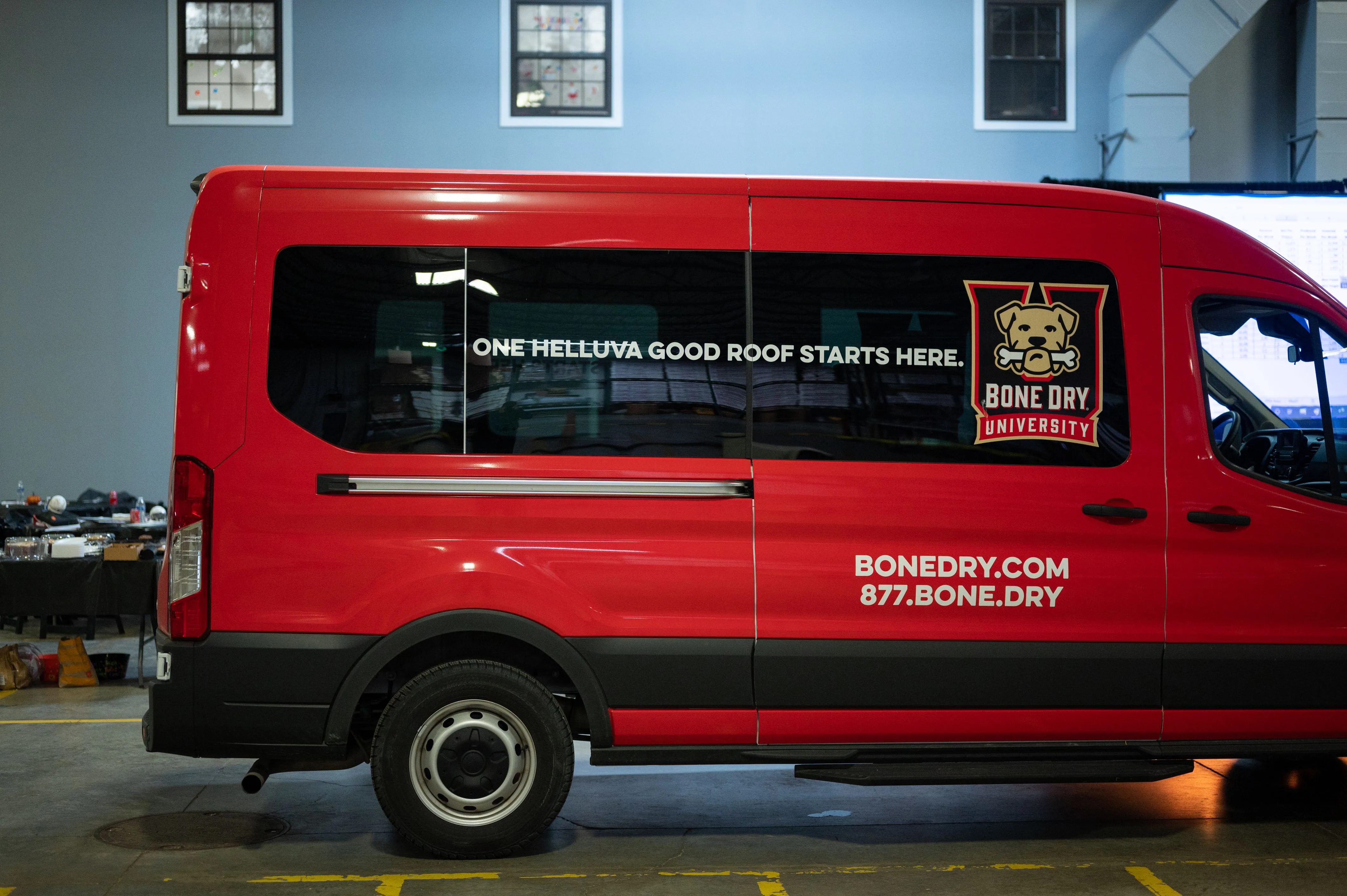 A red delivery van parked inside a building with promotional text and website URL on its side panel.