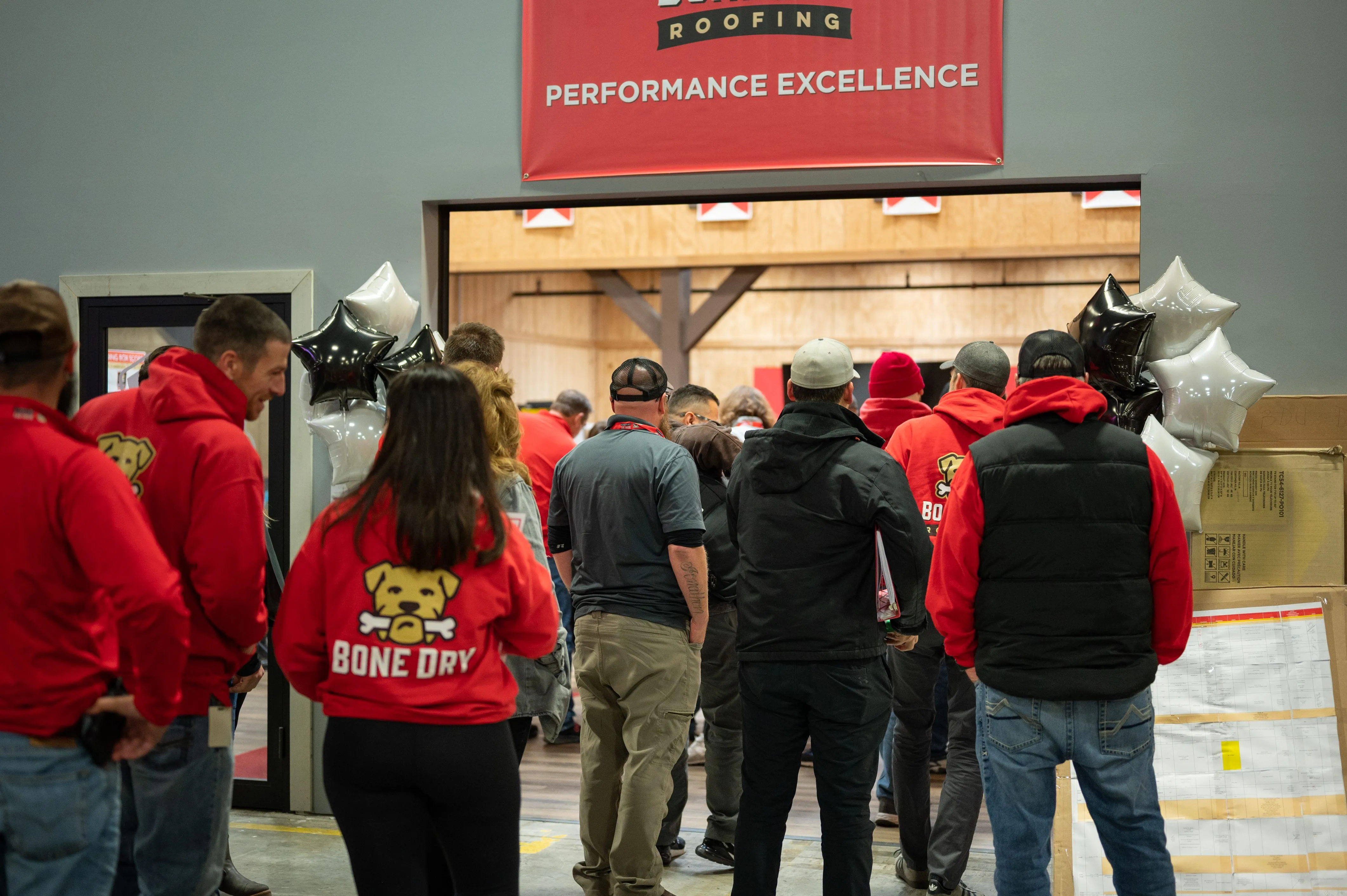 Group of people wearing red attending a trade show booth with a sign reading 'Performance Excellence.'