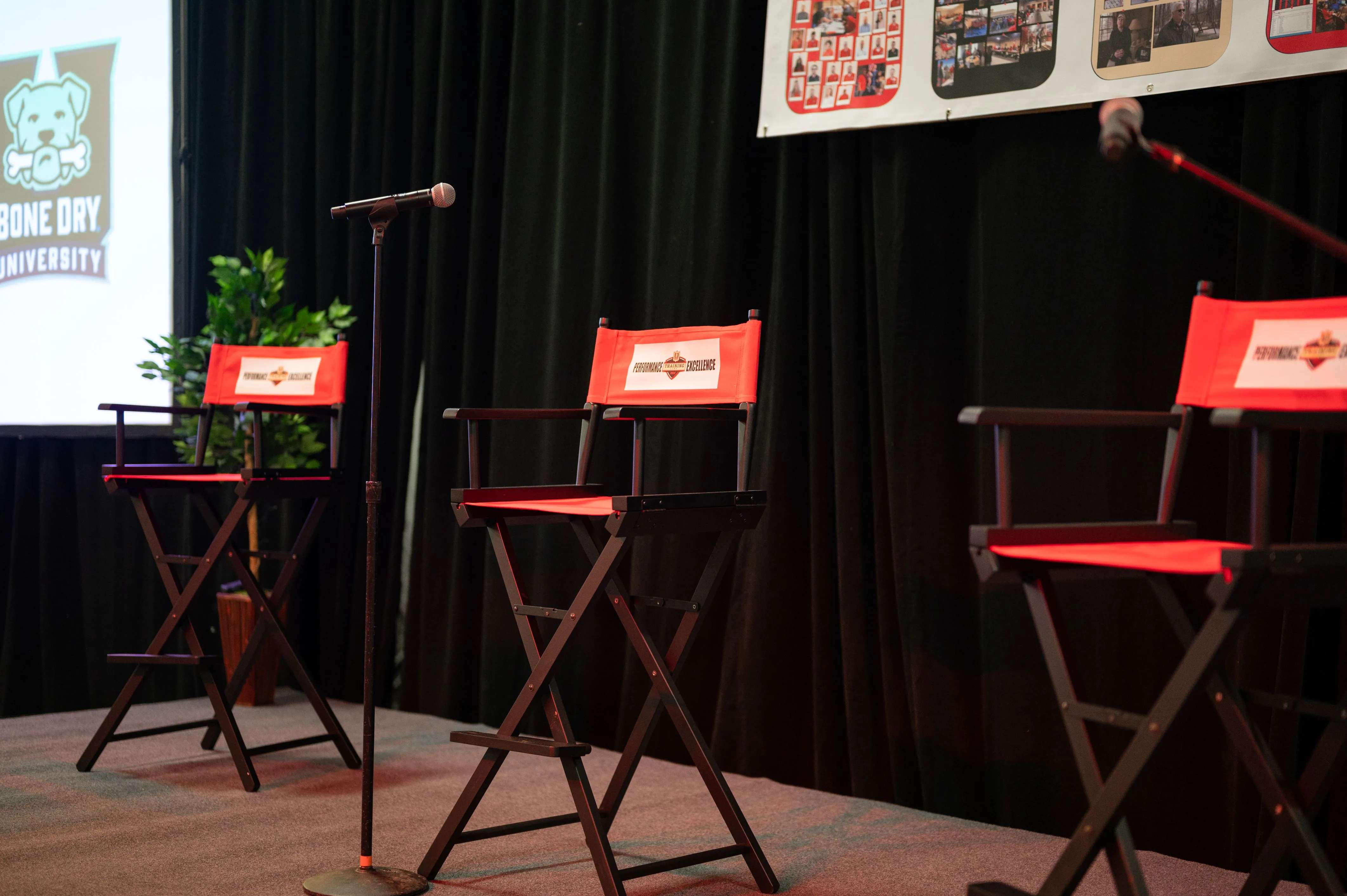  "A stage setup with three empty director's chairs and a microphone, possibly for a panel discussion or interview session."