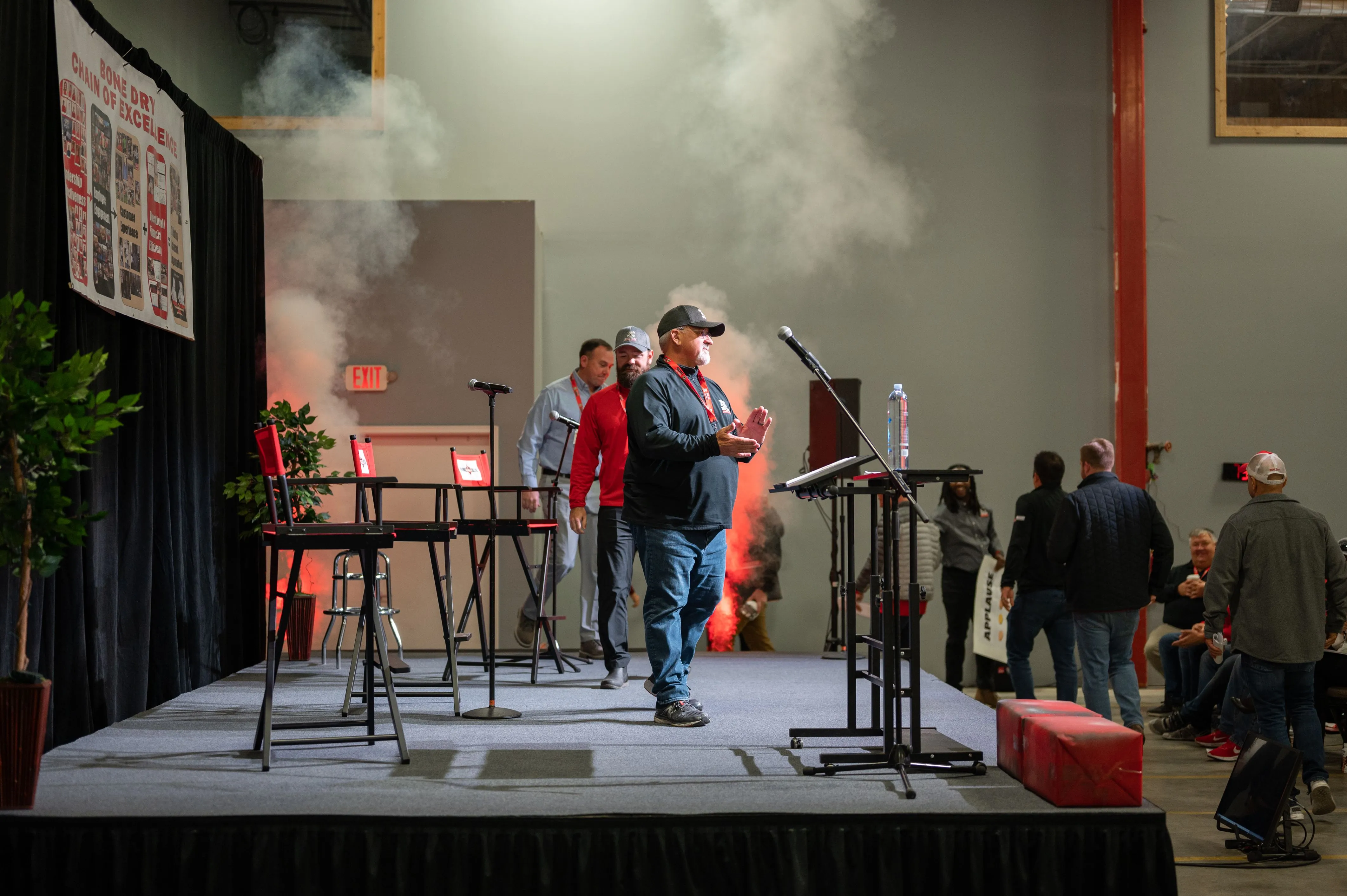 People walking on a stage with musical equipment and smoke effects during an event.