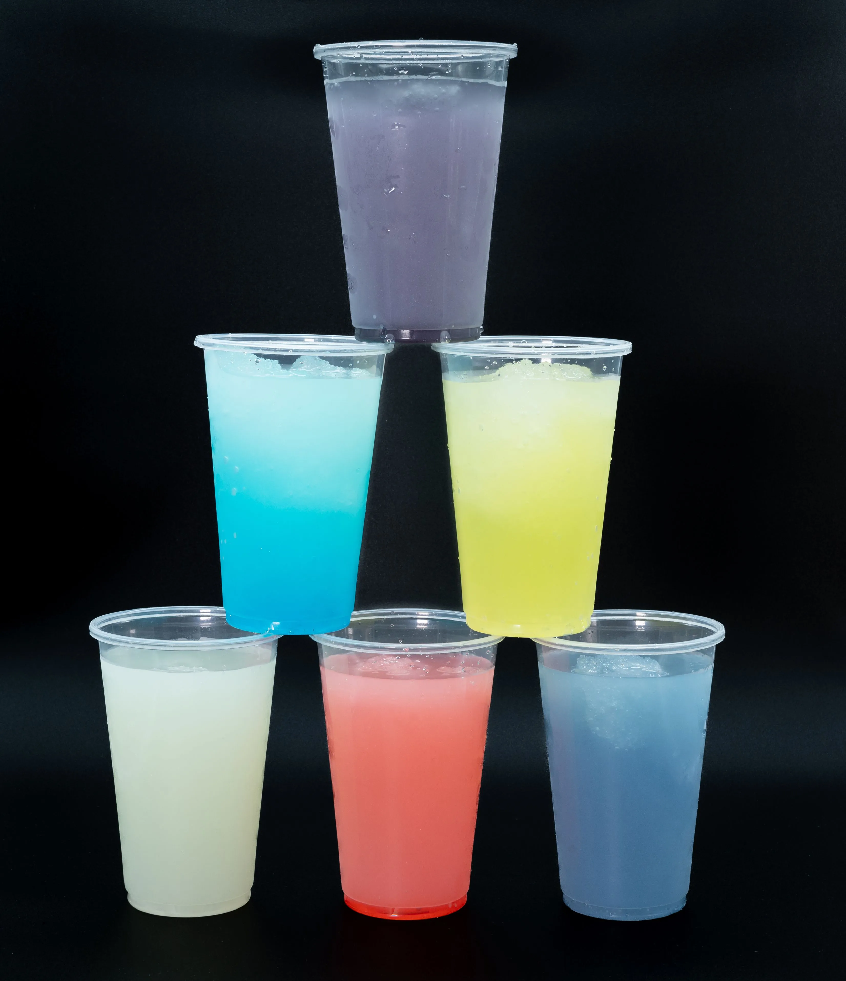 Five colorful frozen drinks in clear plastic cups stacked in a pyramid formation on a black background.