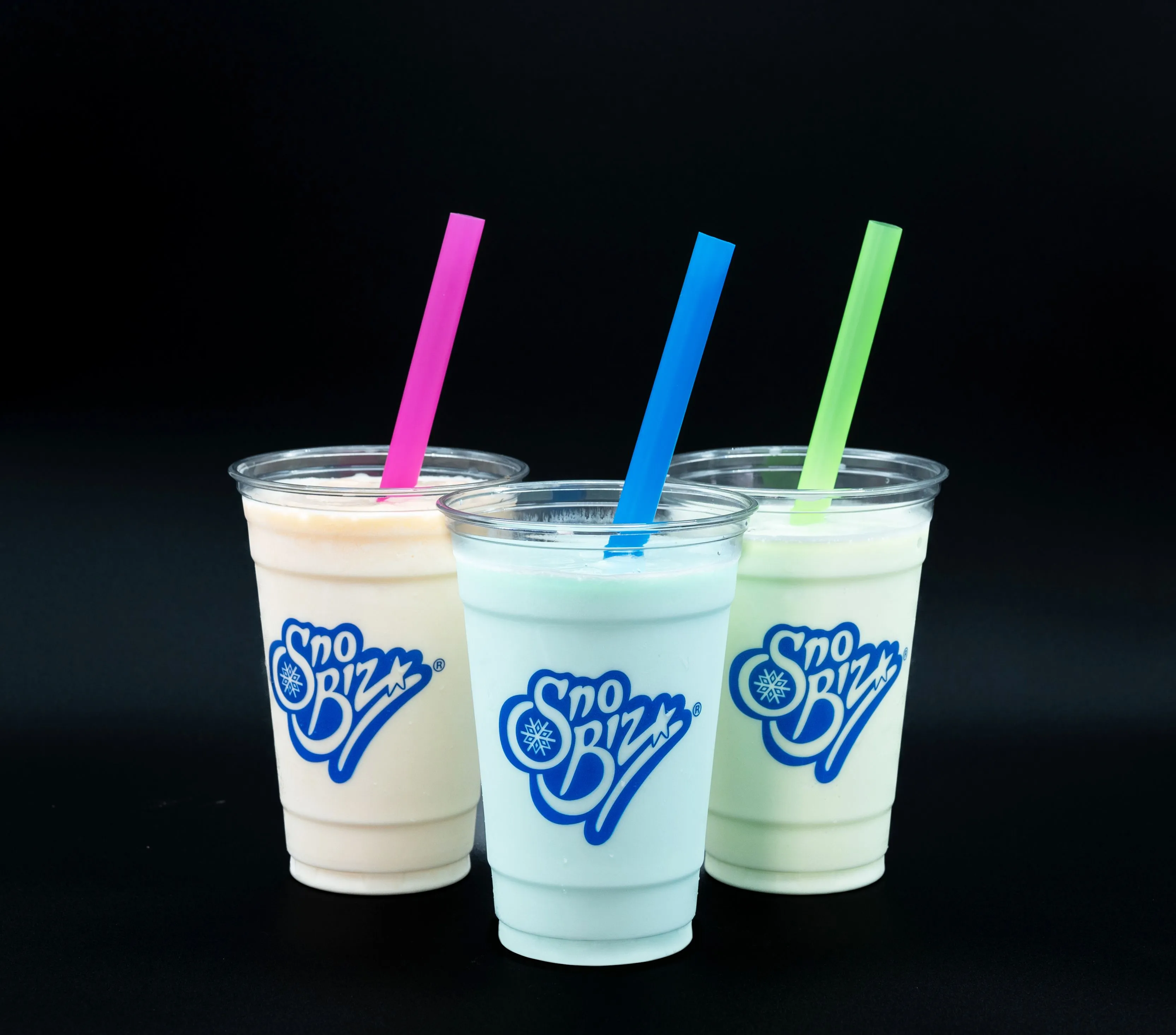 Three Sno Biz branded frozen drinks with pink, blue, and green straws against a black background.