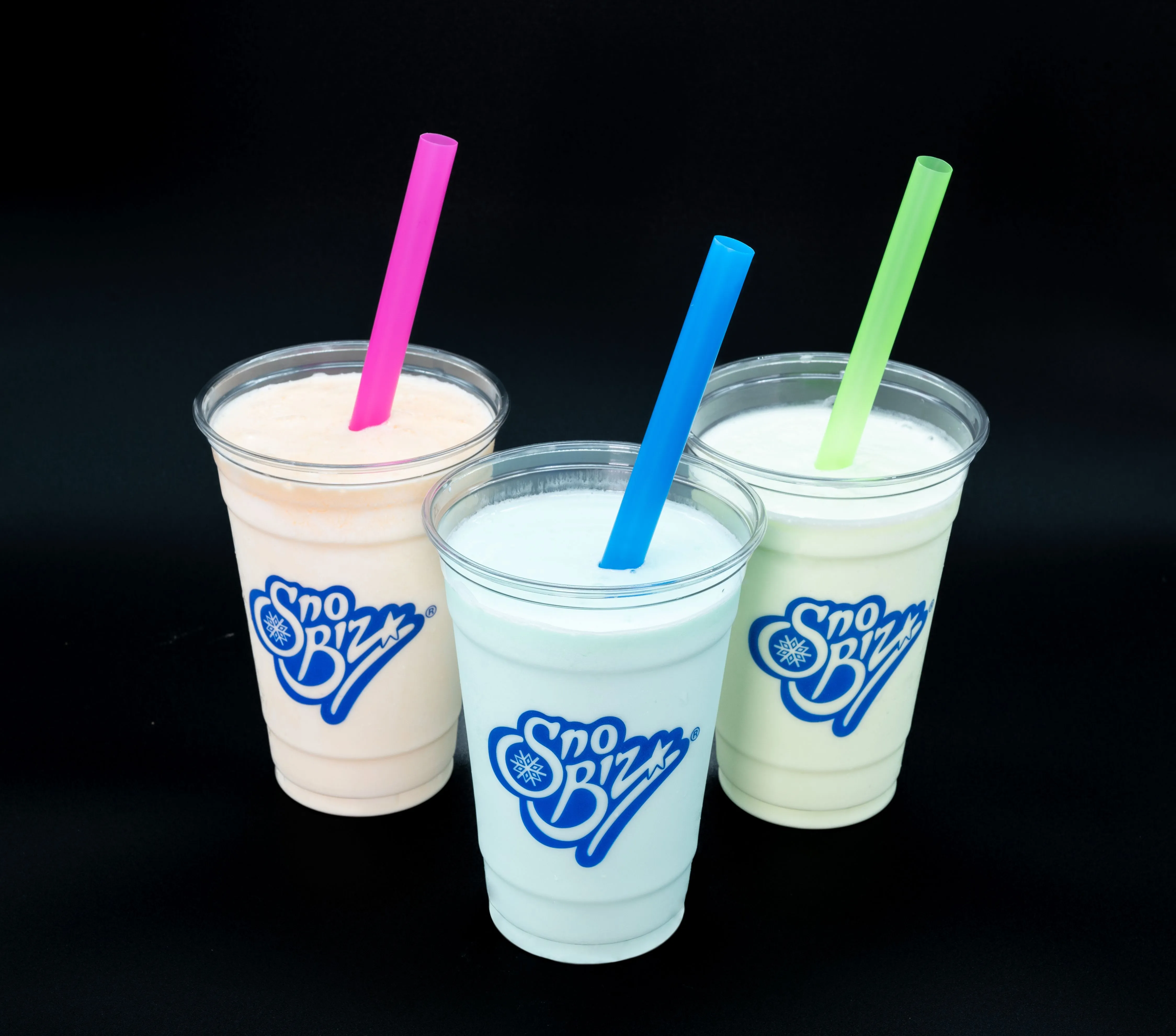 Three Sno Biz branded milkshake cups with pink, blue, and green straws against a black background.