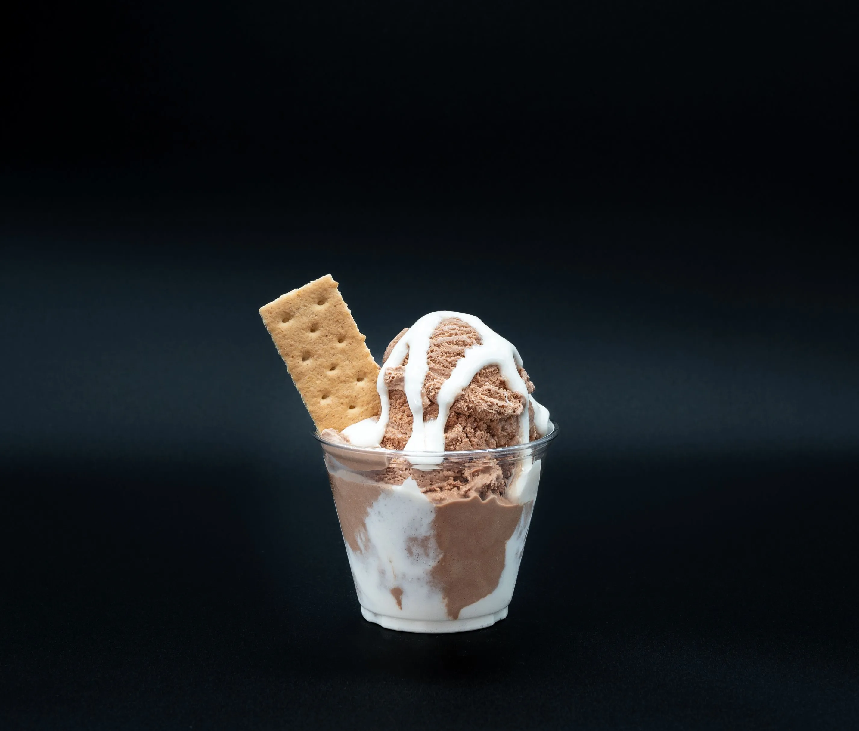 A cup of chocolate and vanilla ice cream with a biscuit stick on a dark background.