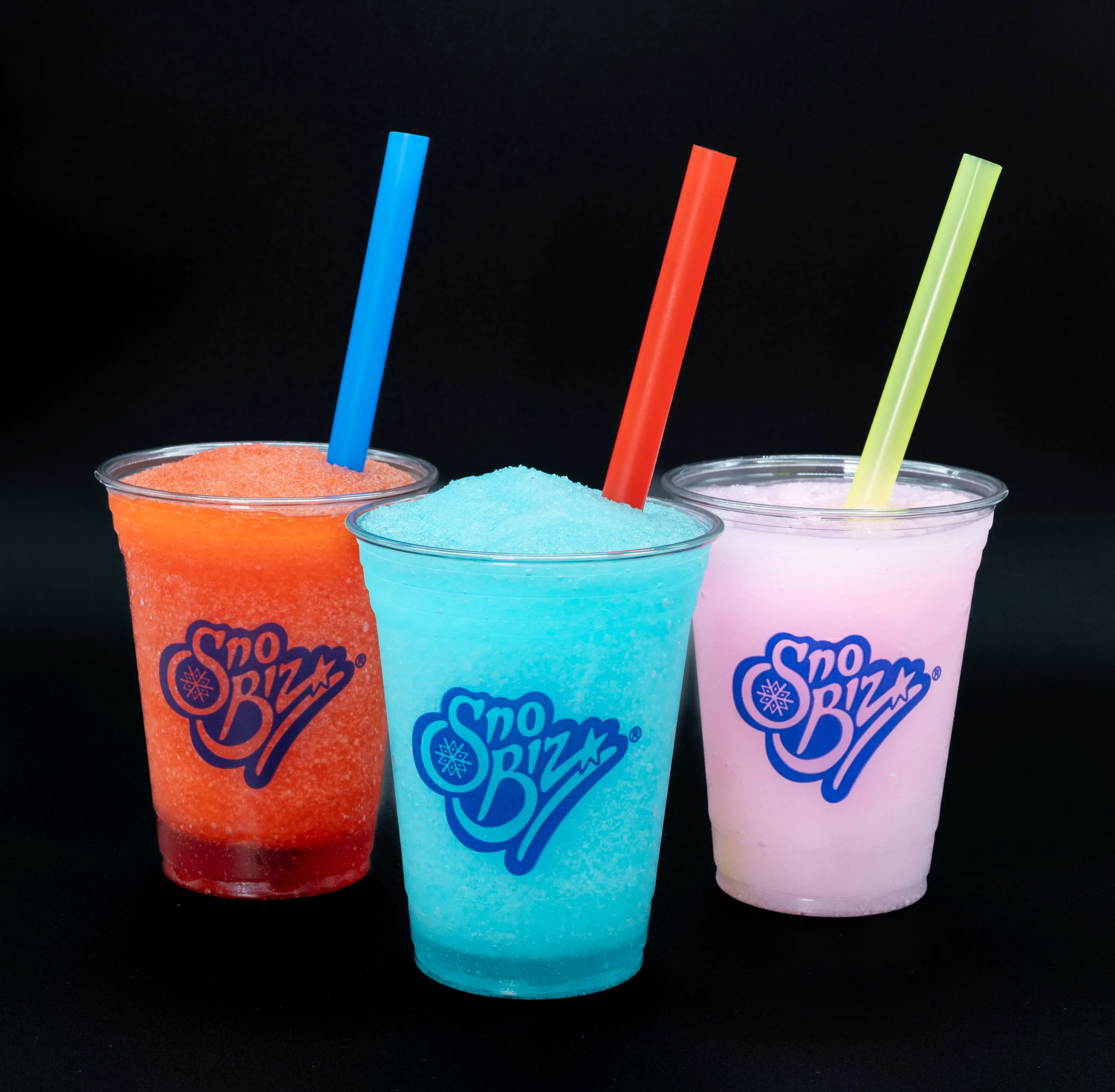 Three colorful Sno Biz shaved ice drinks with straws on a black background.