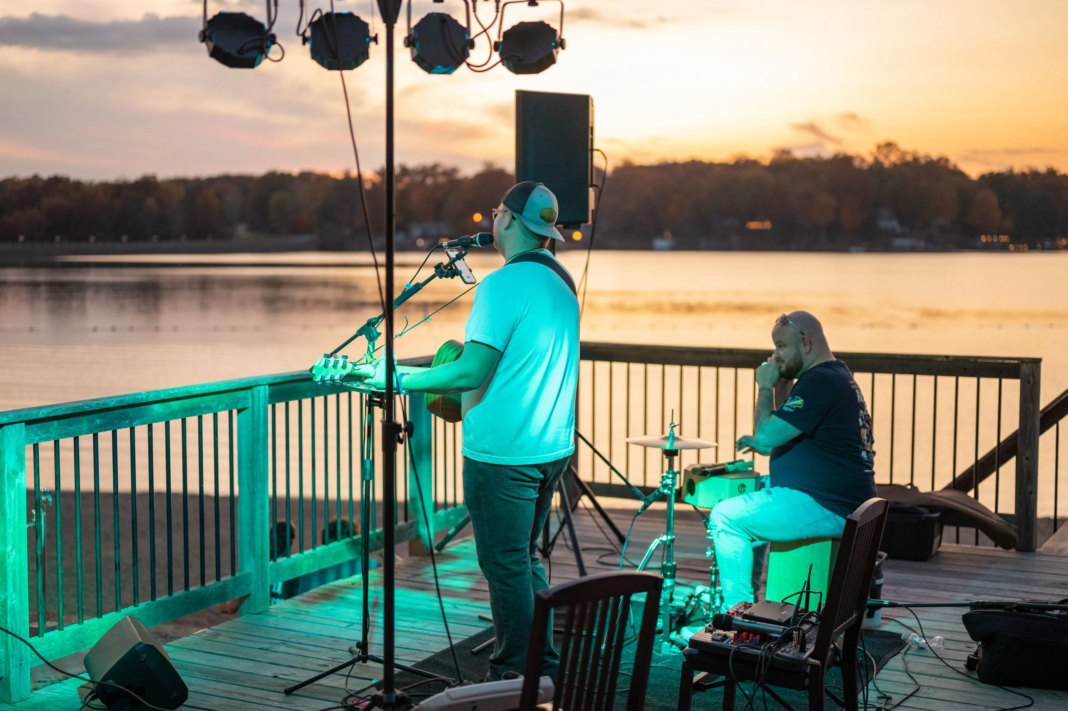 Musician performing on a pier at sunset with a calm lake in the background.