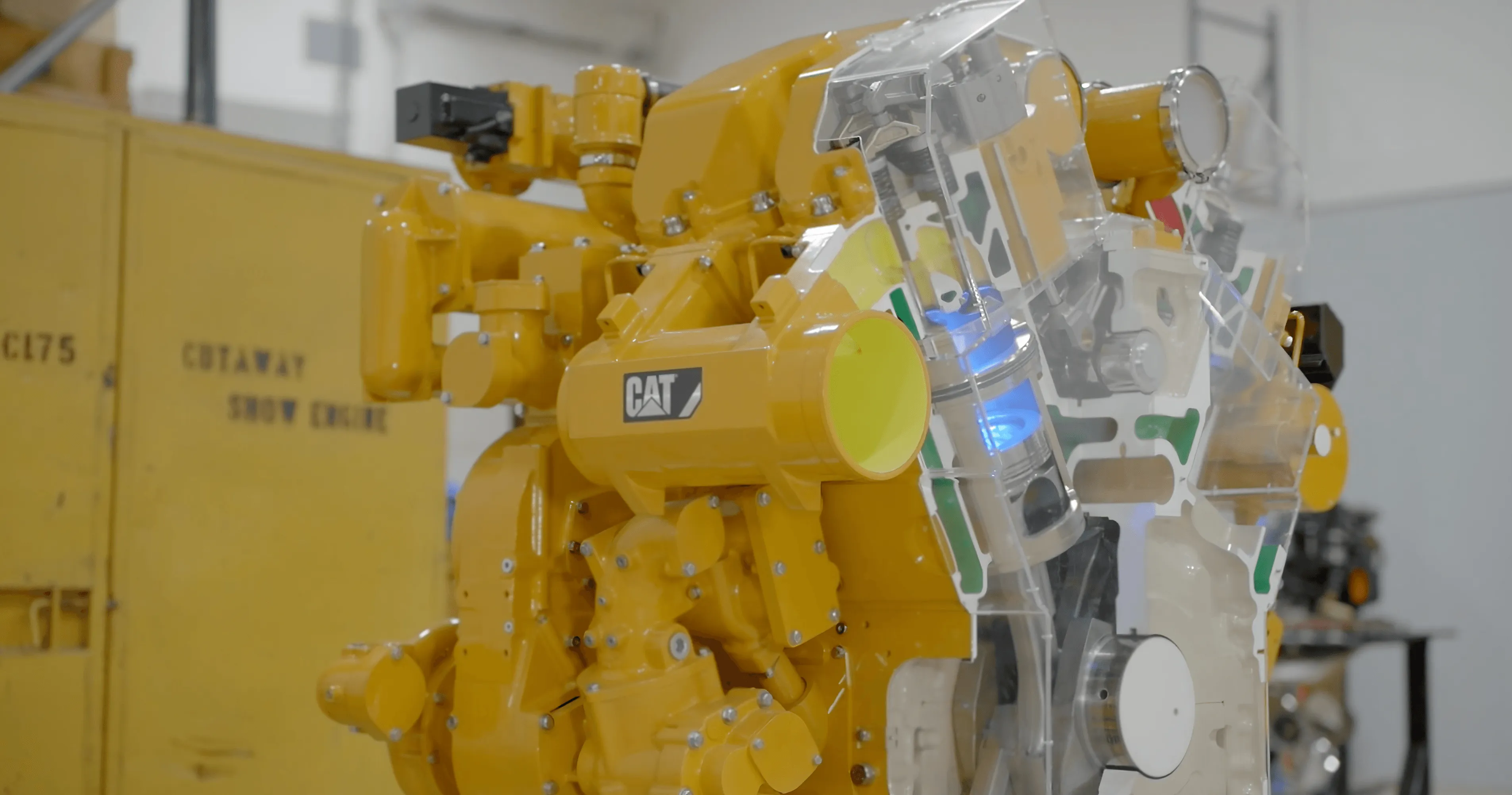 Industrial robot with yellow components and a partially transparent casing on display, with manufacturing equipment in the background.