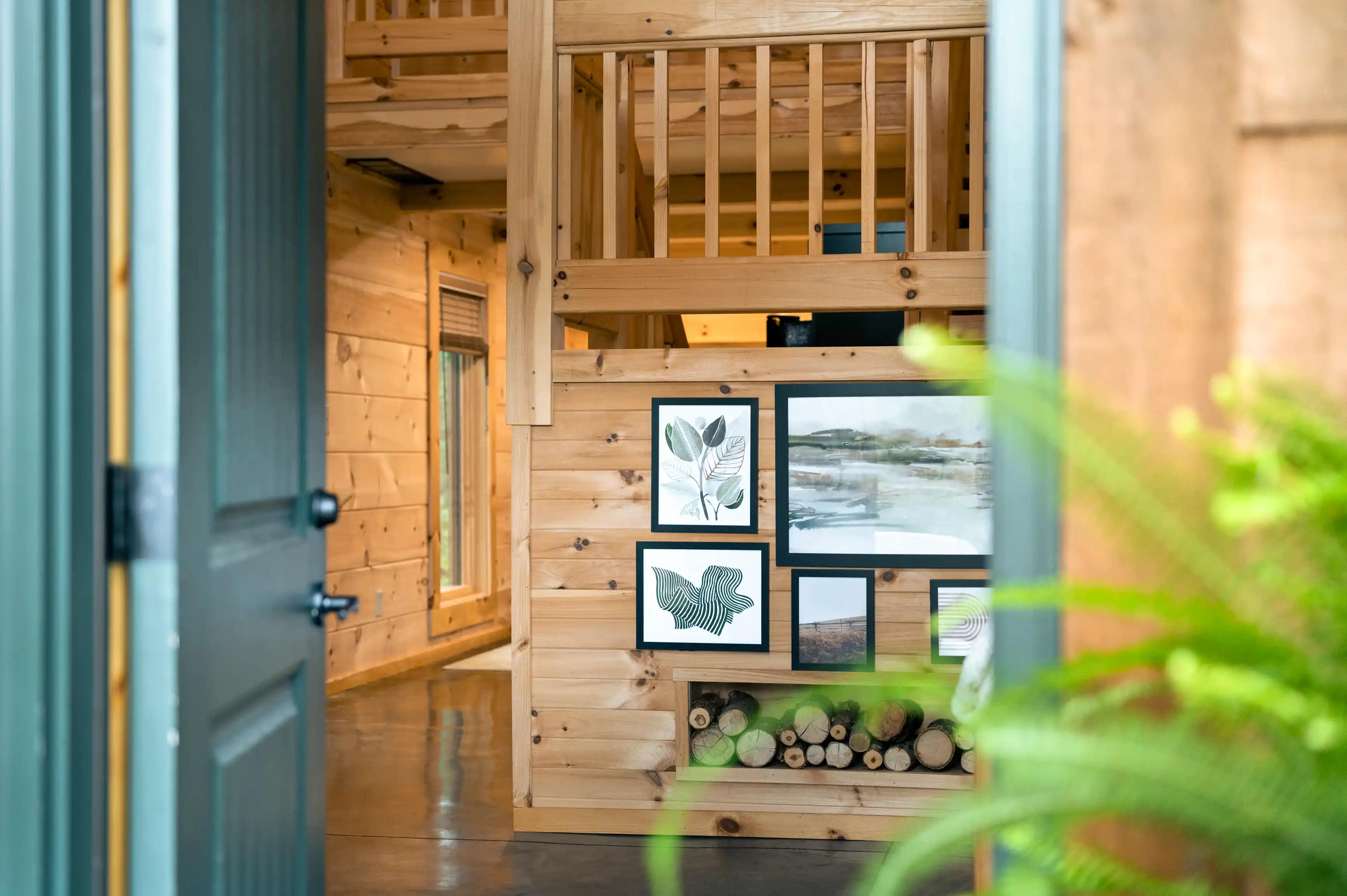 Interior view of a cozy wooden cabin with framed artwork on the wall, visible through an open door, with a focus on natural light and simplicity.