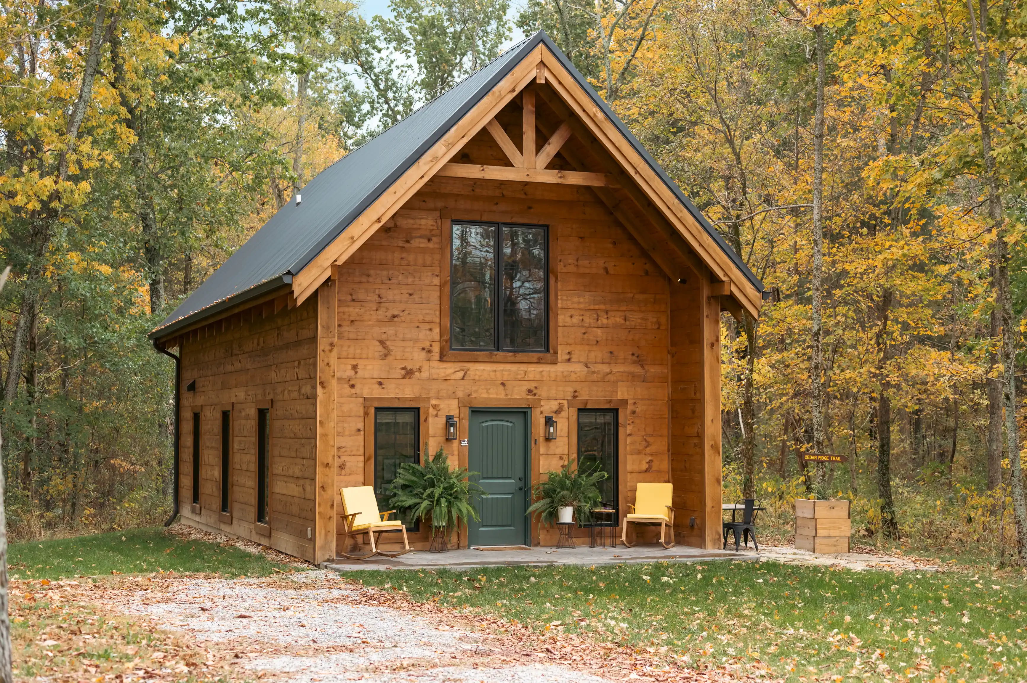A wooden cabin with a gabled roof and a front porch surrounded by trees with autumn foliage.