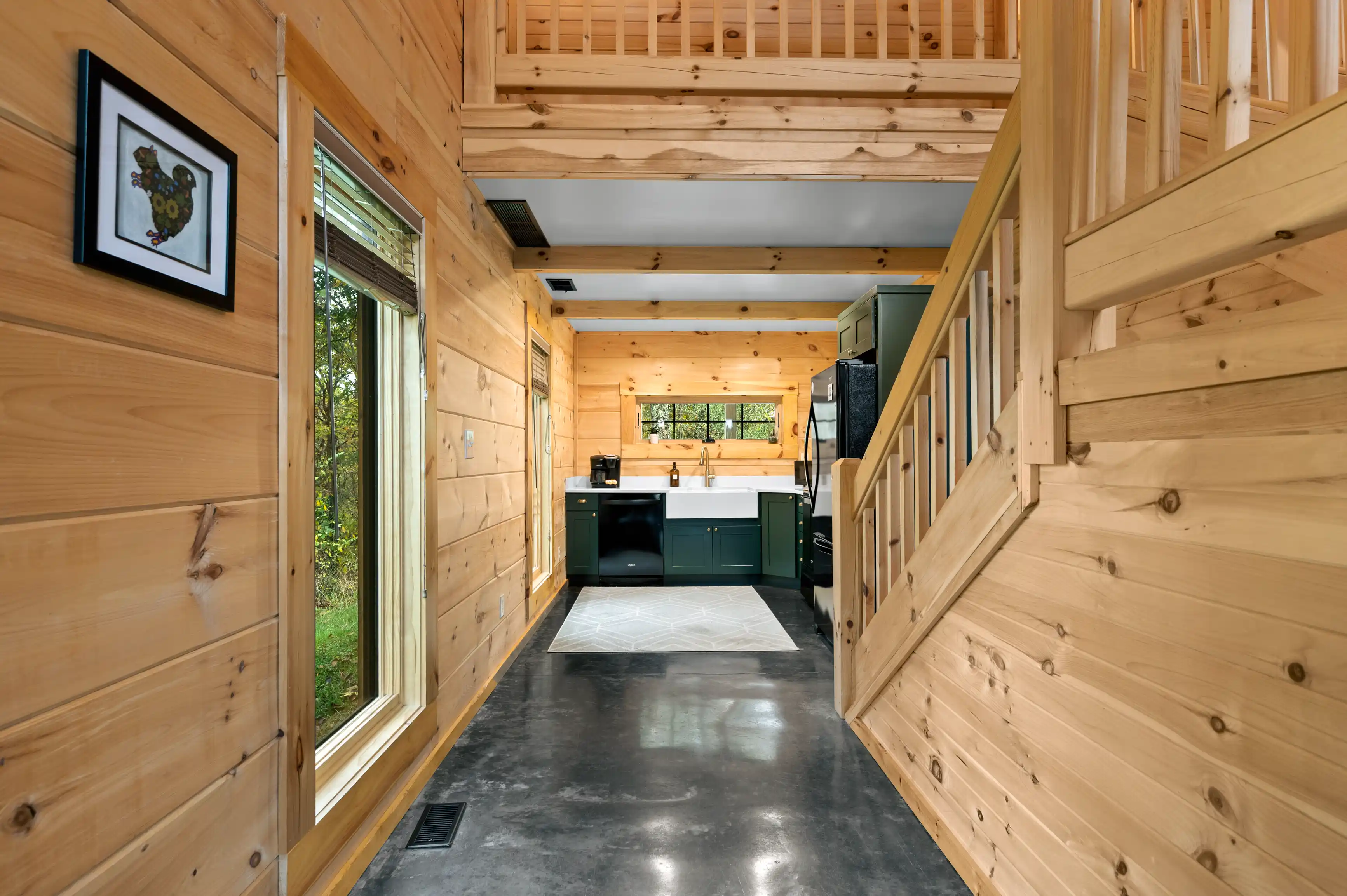 Interior of a modern tiny house with wooden walls, a loft bedroom, and a kitchen area with green cabinets.