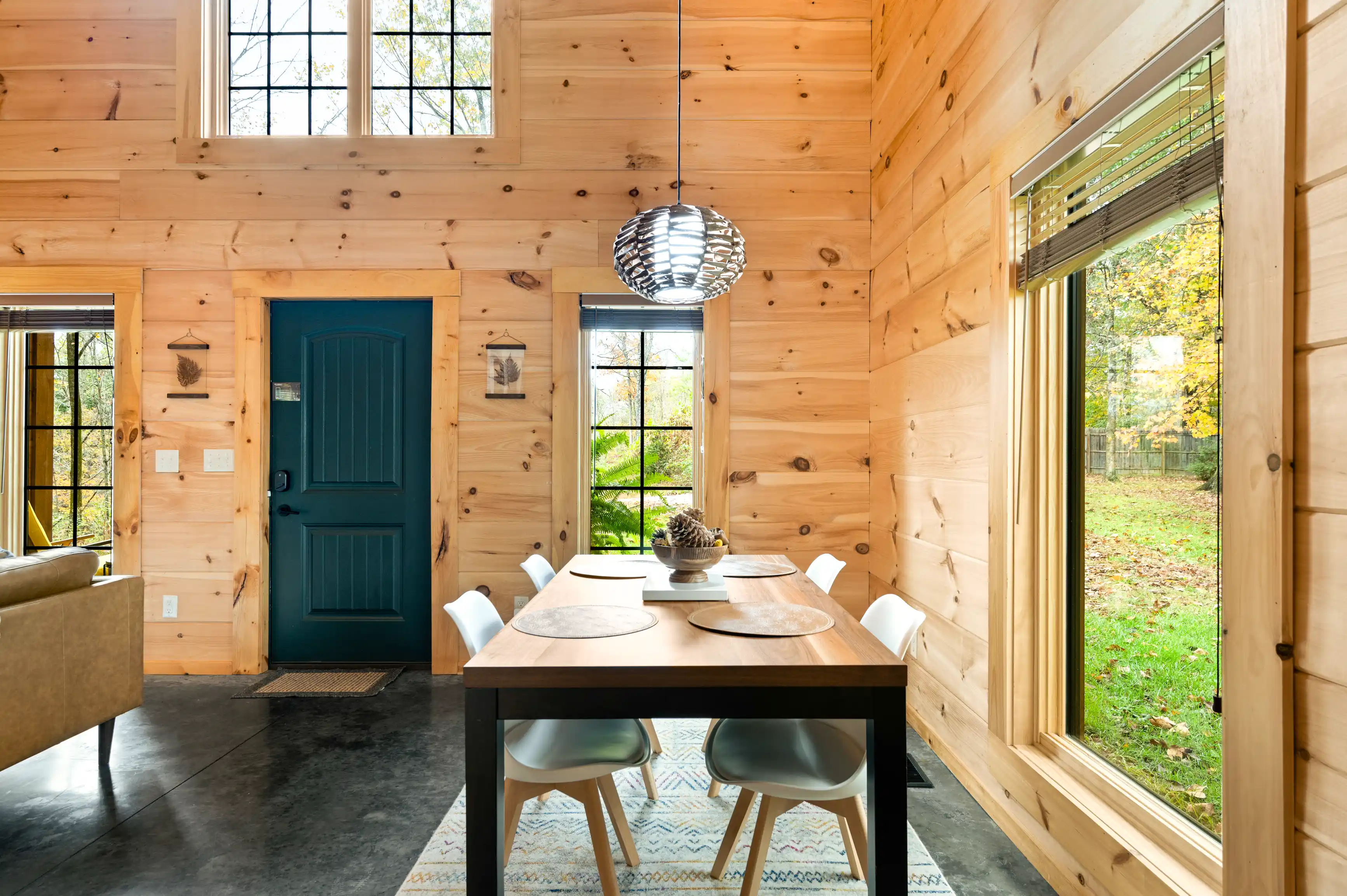 Cozy wooden cabin interior with a dining table, chairs, and a view of the outdoors through large windows.