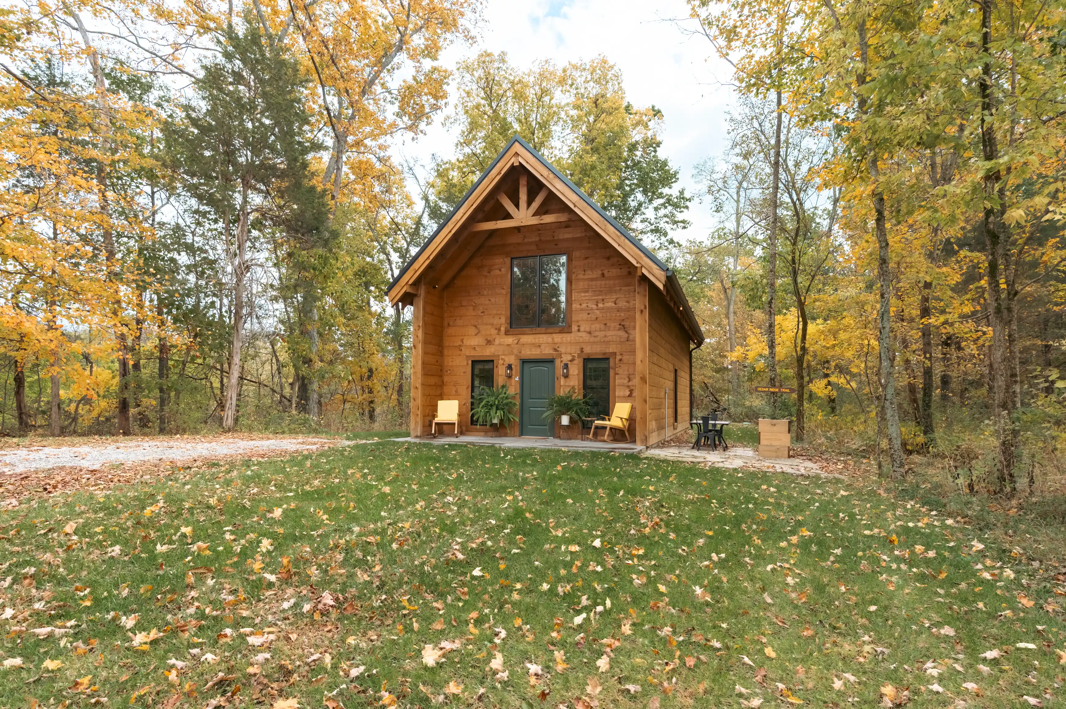 A cozy wooden cabin surrounded by autumnal trees with fallen leaves on the ground.