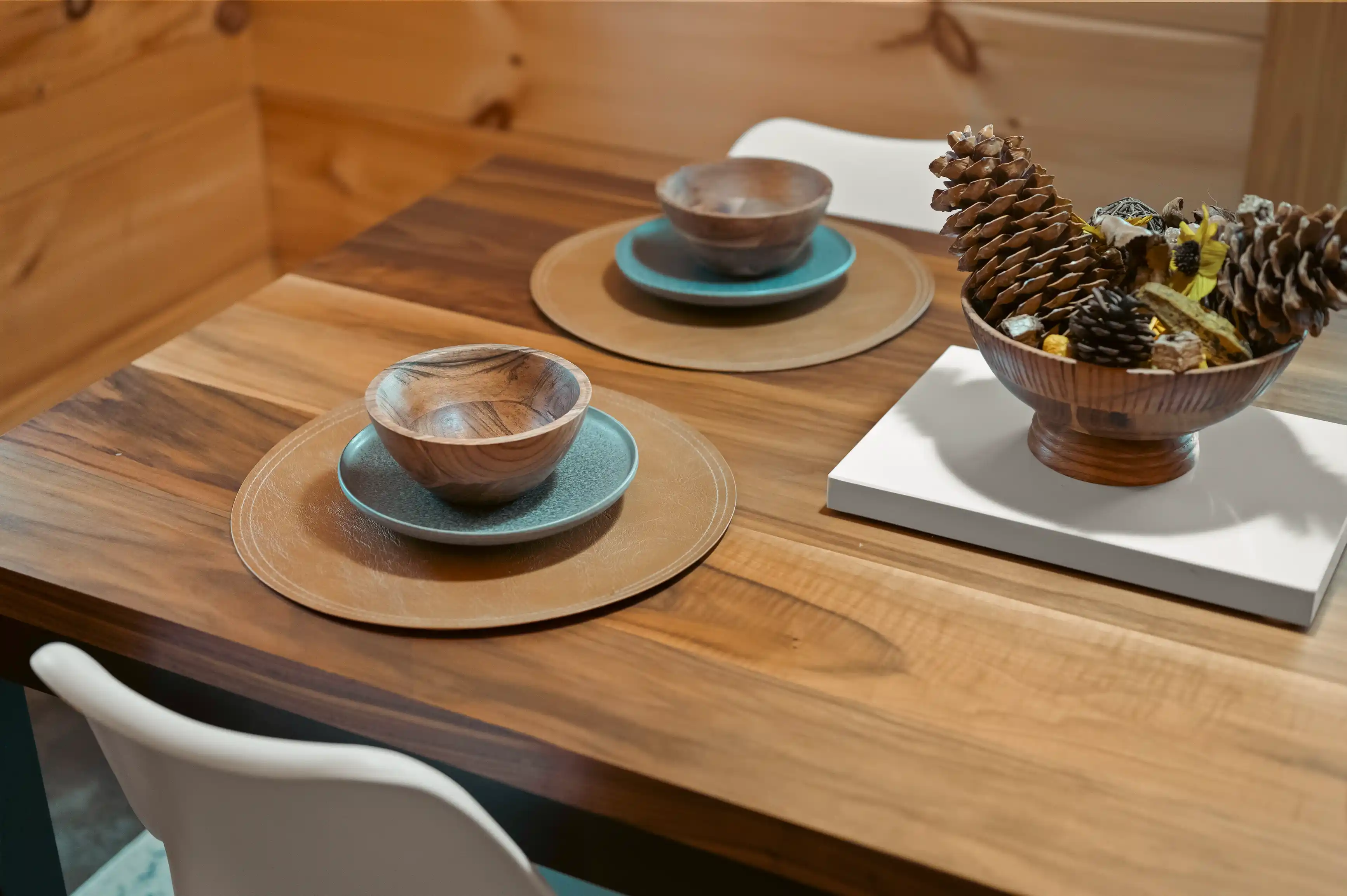 Wooden dining table set with plates, bowls, and a decorative centerpiece containing pine cones.