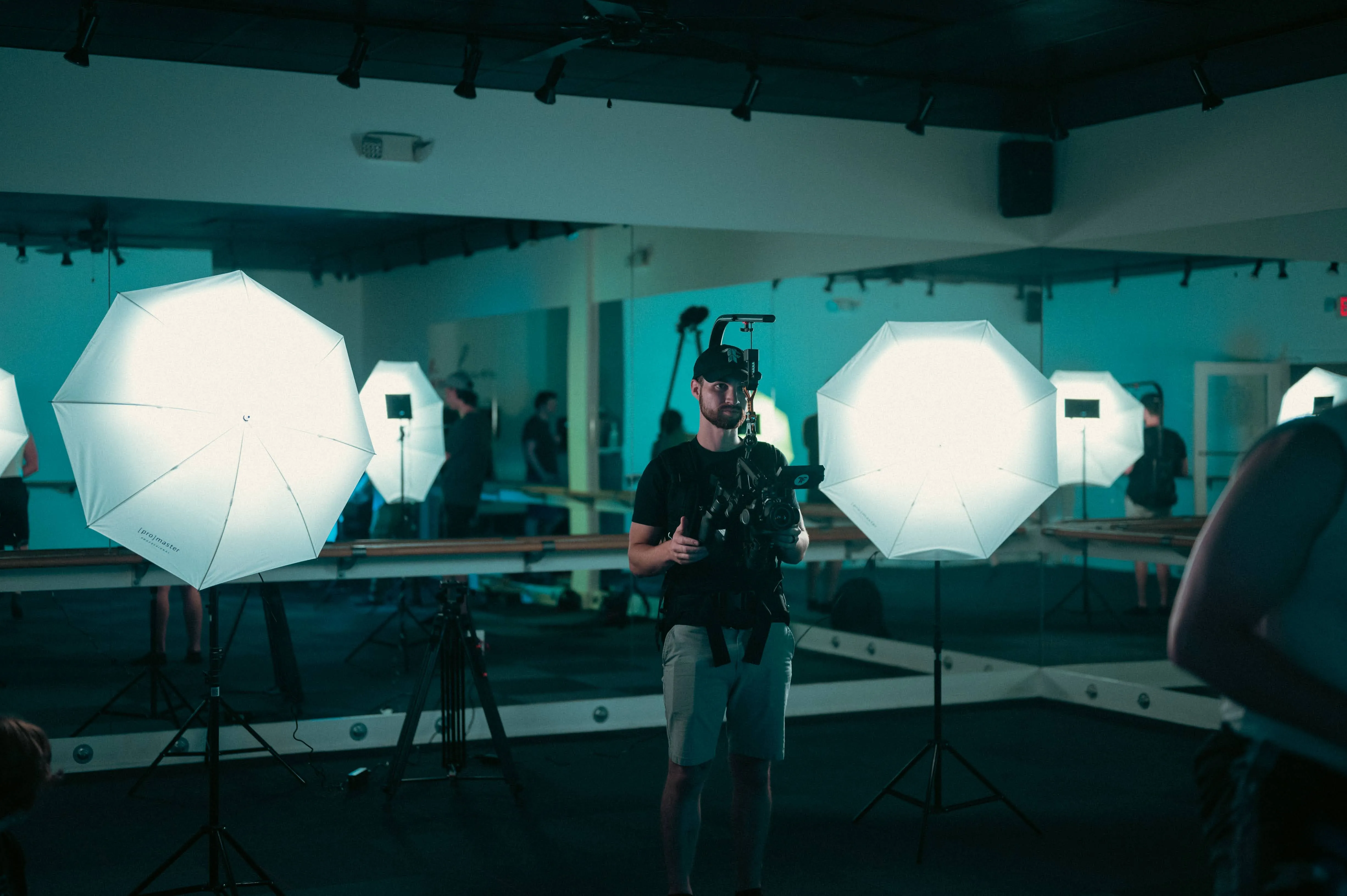 A photographer working in a studio with multiple umbrella lights set up around him.