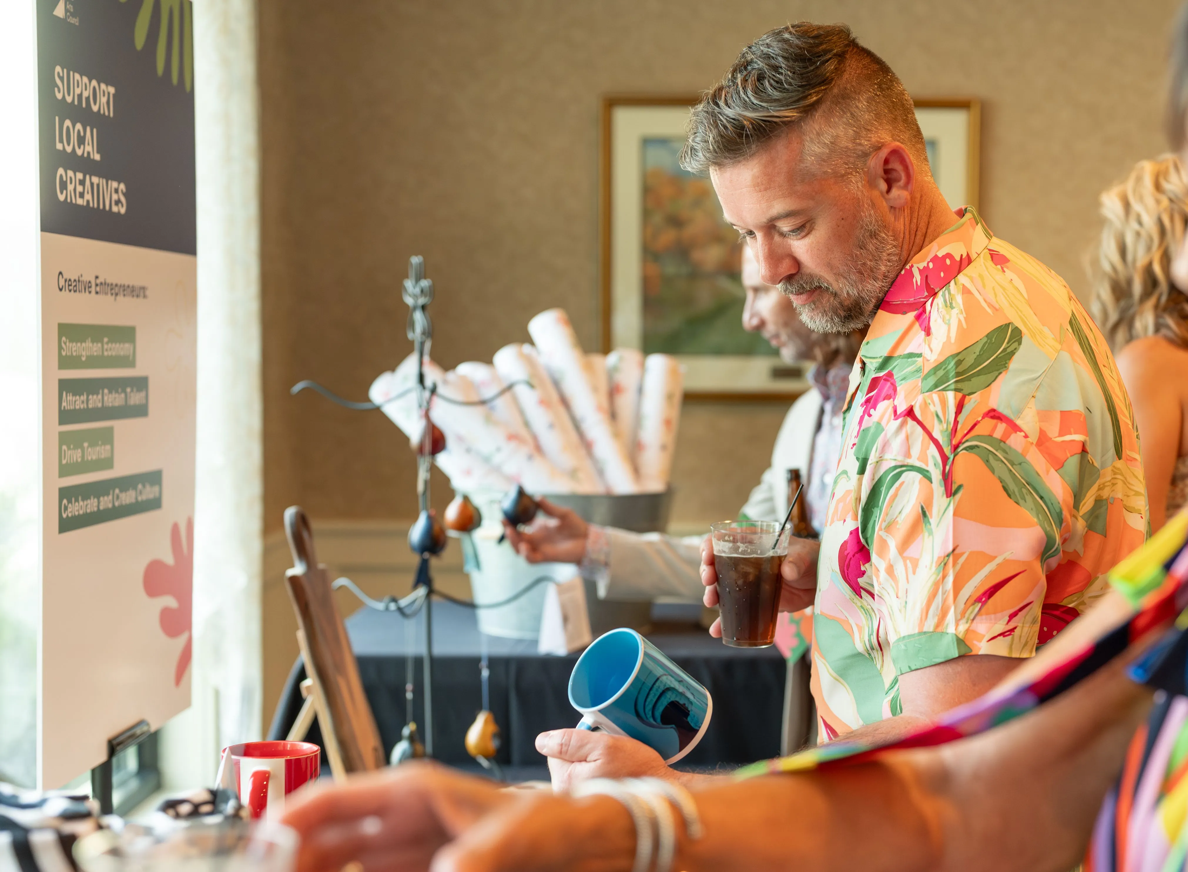 Man in a colorful shirt examining a piece of jewelry with tools at a workshop table.