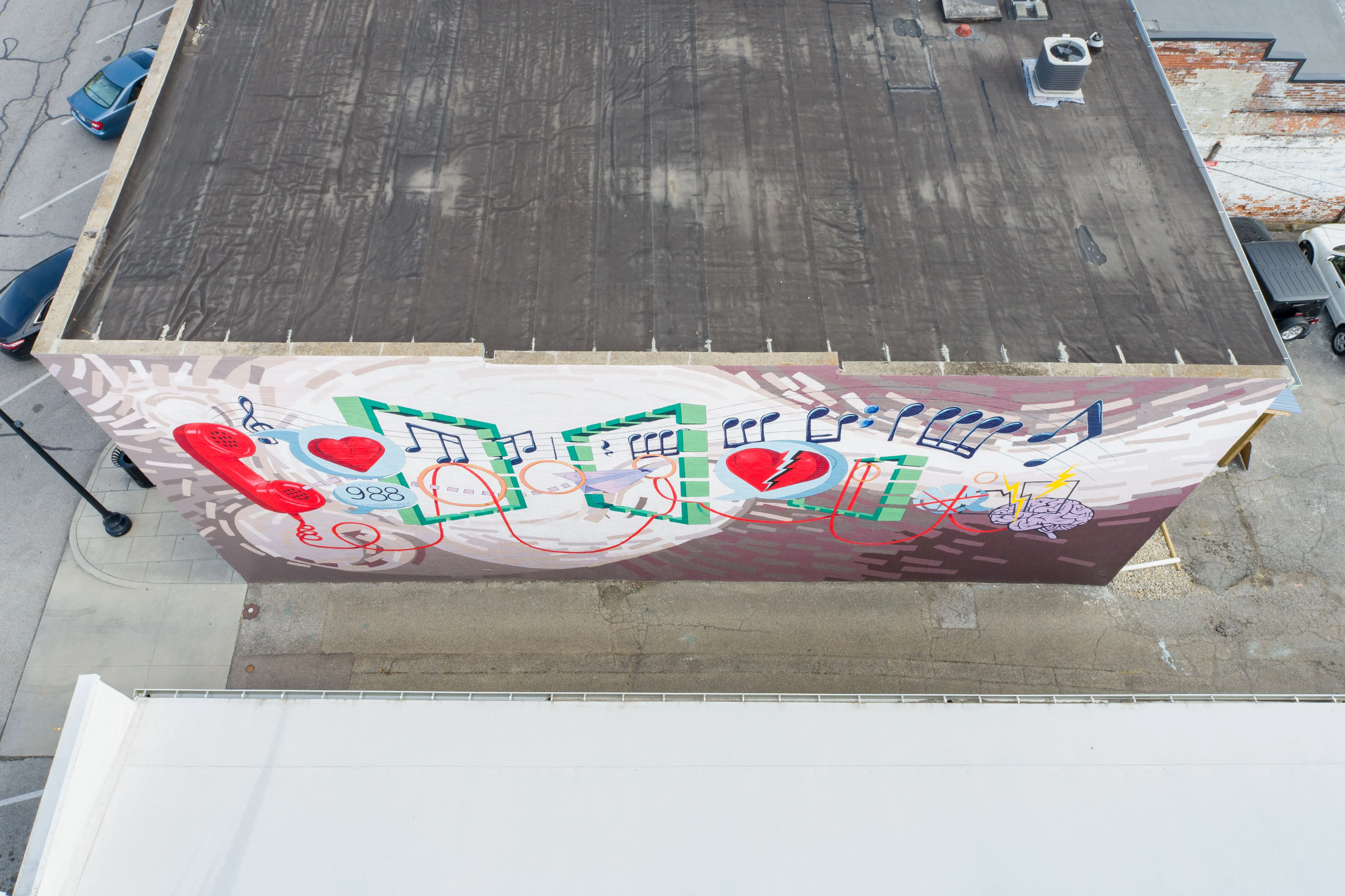 Aerial view of a building with a colorful mural on its rooftop featuring hearts and geometric patterns.